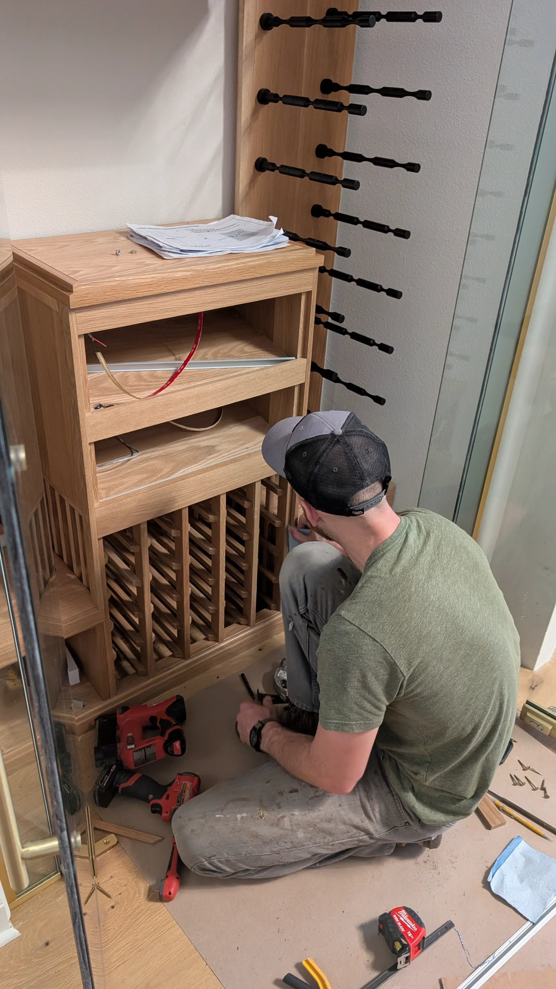 A high-end custom white oak wine cellar under construction featuring modern black metal wine pegs and glass-enclosed shelving for a luxury home project in West Lake Hills, Austin. - Detail 2
