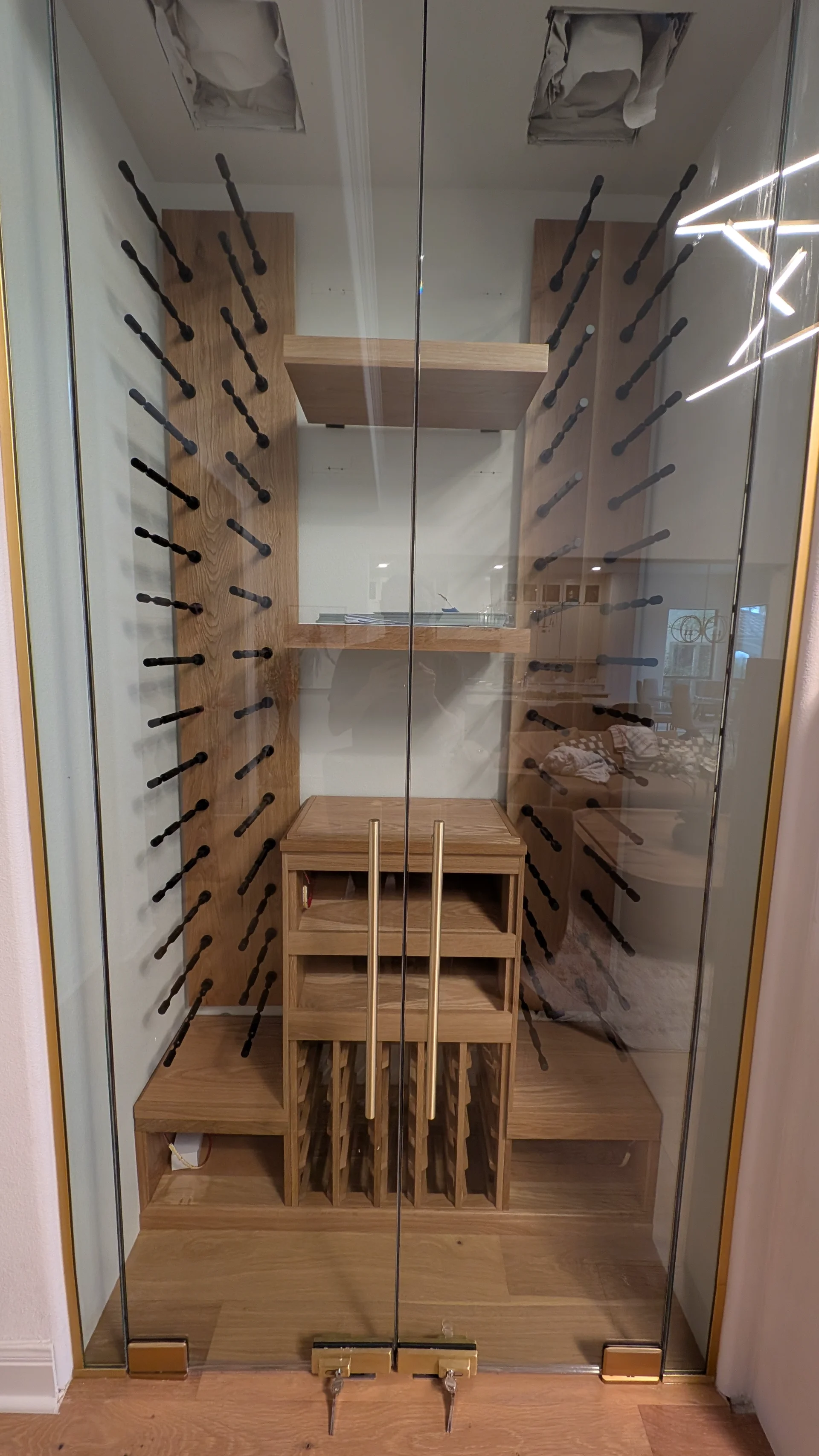 A high-end custom white oak wine cellar under construction featuring modern black metal wine pegs and glass-enclosed shelving for a luxury home project in West Lake Hills, Austin. - Detail 3