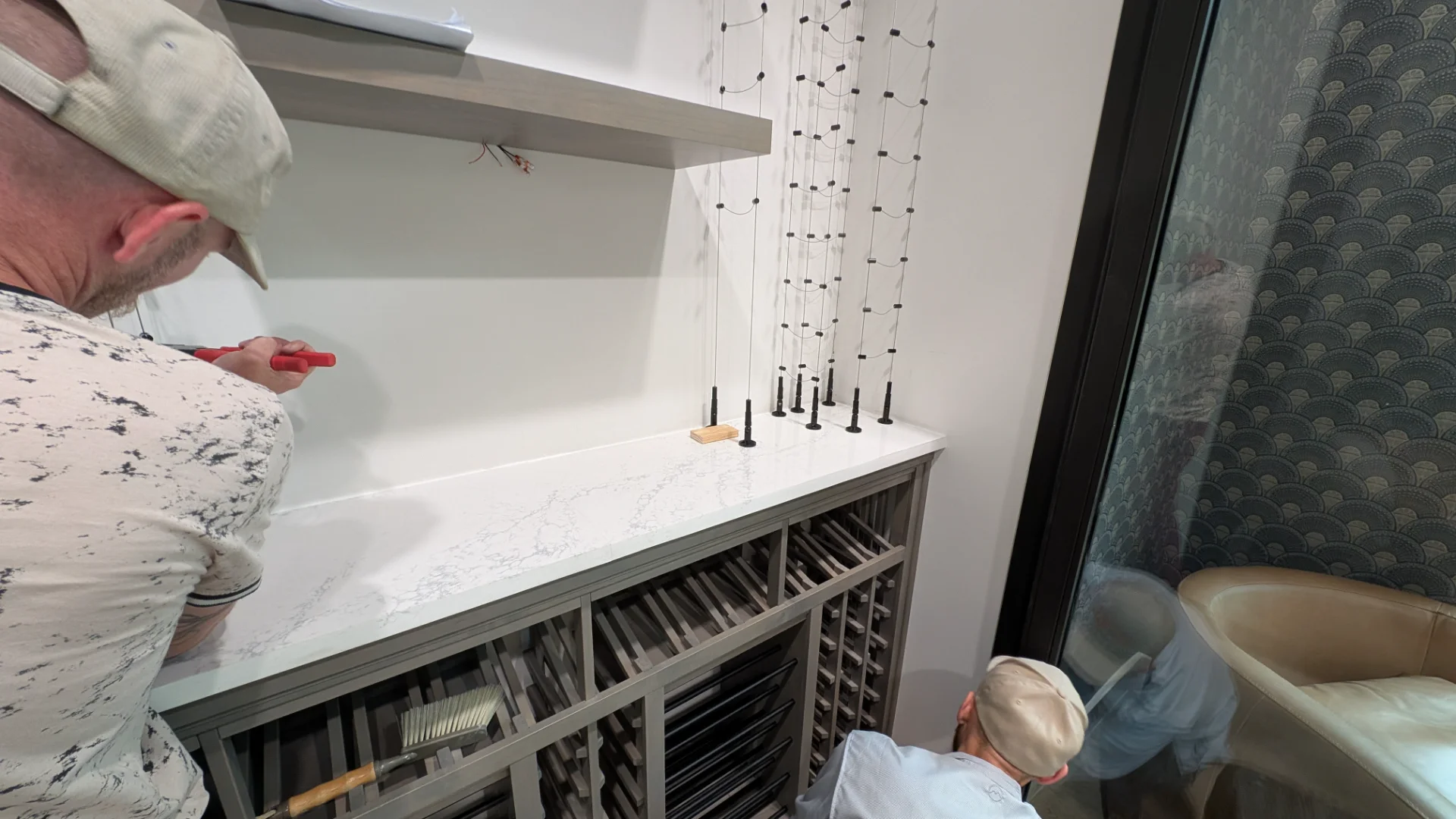 A luxury glass-enclosed wine cellar featuring custom wooden storage and cable wine racks, set against an Art Deco patterned wallpaper in a modern Austin, Texas home. - Detail 2