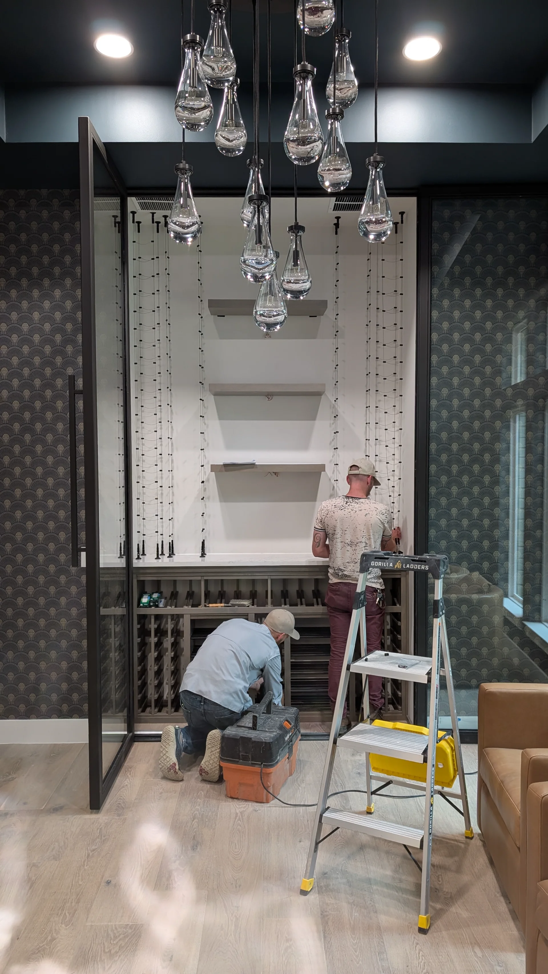 A luxury glass-enclosed wine cellar featuring custom wooden storage and cable wine racks, set against an Art Deco patterned wallpaper in a modern Austin, Texas home. - Detail 3