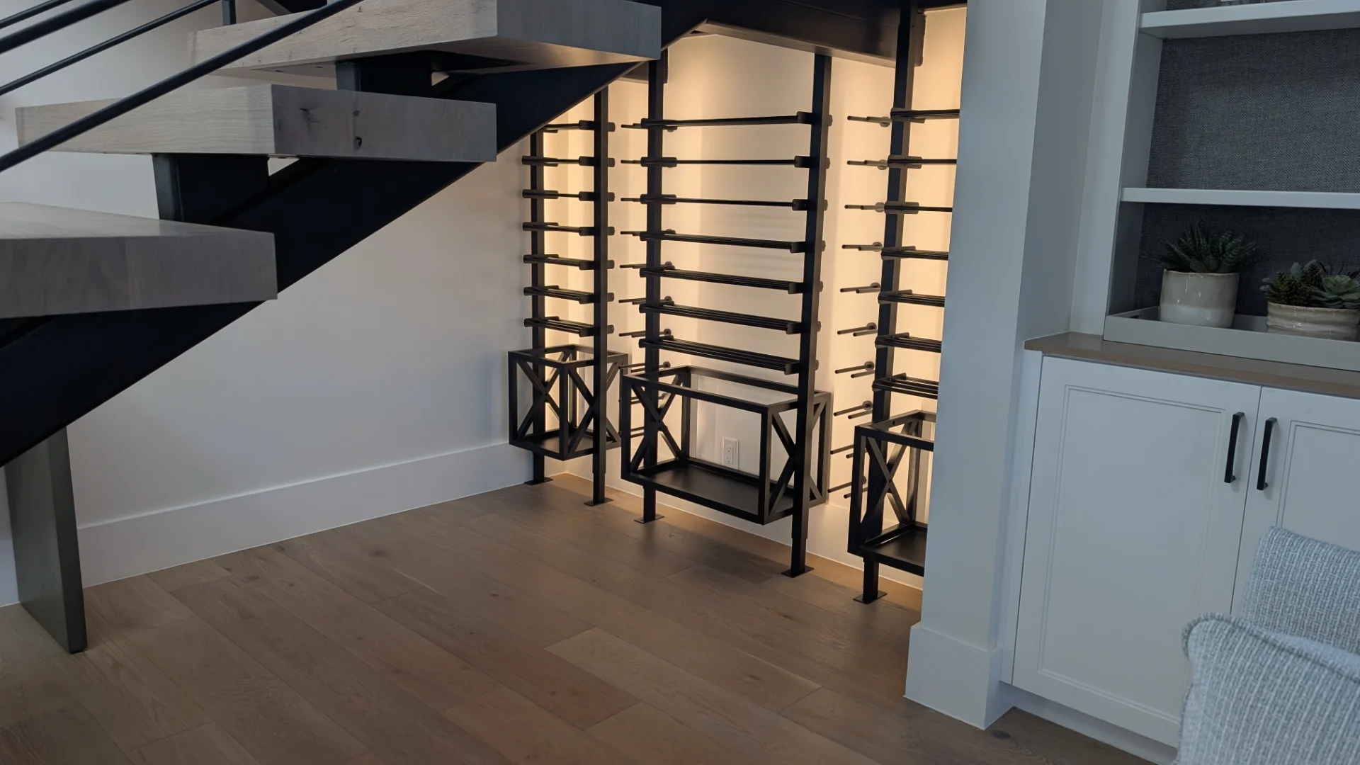 A custom-designed modern black metal wine rack with sophisticated backlighting, installed in a luxury home bar area in Austin, featuring dark wood ceiling beams and sleek cabinetry. - Detail 3