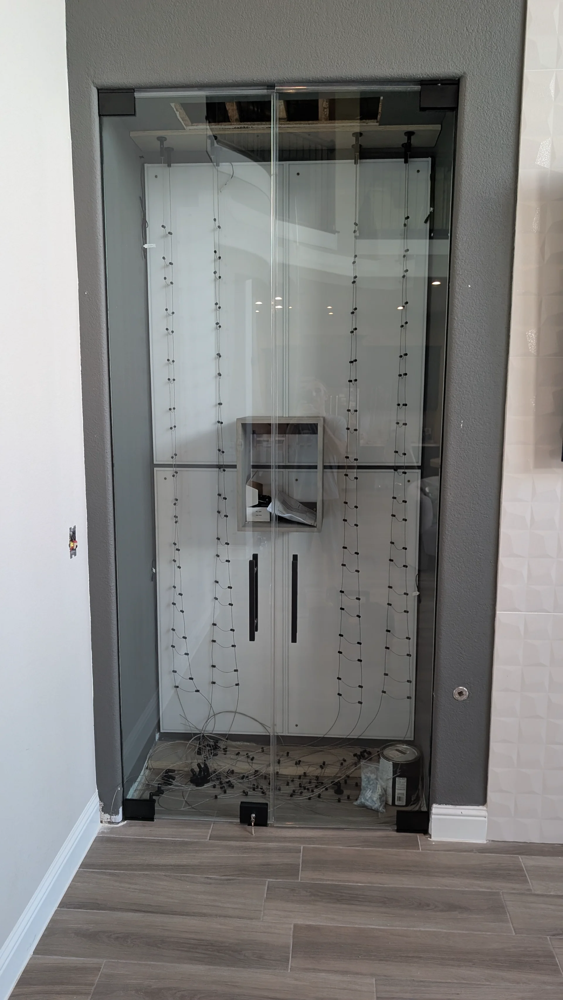 A high-end, contemporary glass wine cellar with a glowing, backlit frosted panel and a vertical cable racking system. This sleek architectural feature is part of a custom home project in Austin, West Lake Hills, and the Texas Hill Country. - Detail 2