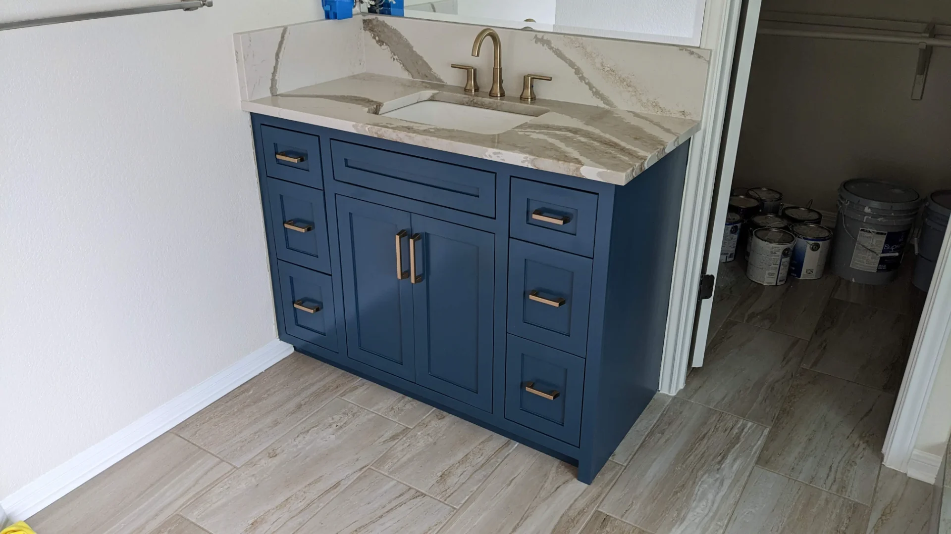 A modern two-tone kitchen remodel in Austin, Texas, showcasing off-white upper cabinets and deep teal lower cabinets with black hardware. The design features marble-patterned quartz countertops and backsplash, a central island, and recessed lighting in a Tarrytown home. - Detail 7