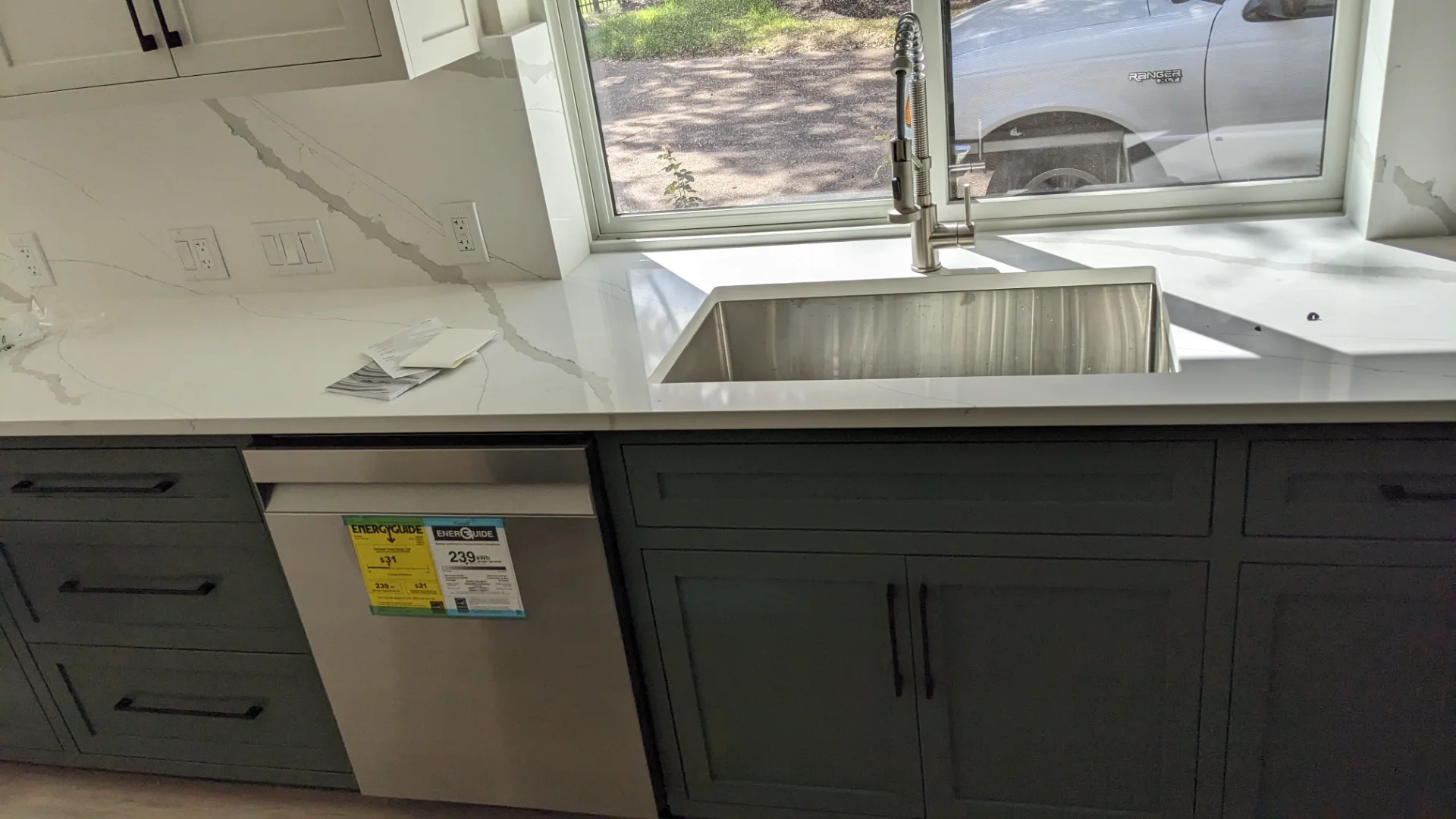 A modern two-tone kitchen remodel in Austin, Texas, showcasing off-white upper cabinets and deep teal lower cabinets with black hardware. The design features marble-patterned quartz countertops and backsplash, a central island, and recessed lighting in a Tarrytown home. - Detail 10