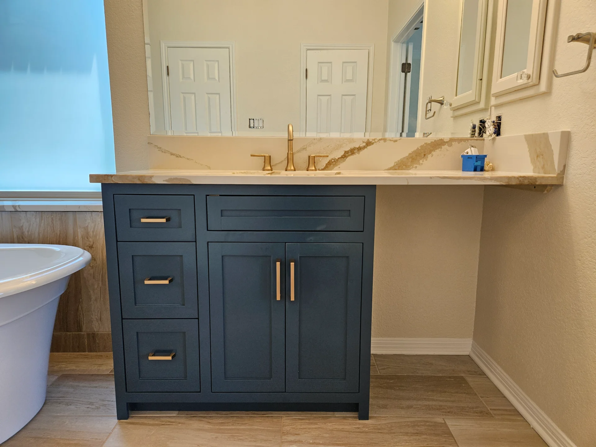A modern two-tone kitchen remodel in Austin, Texas, showcasing off-white upper cabinets and deep teal lower cabinets with black hardware. The design features marble-patterned quartz countertops and backsplash, a central island, and recessed lighting in a Tarrytown home. - Detail 2