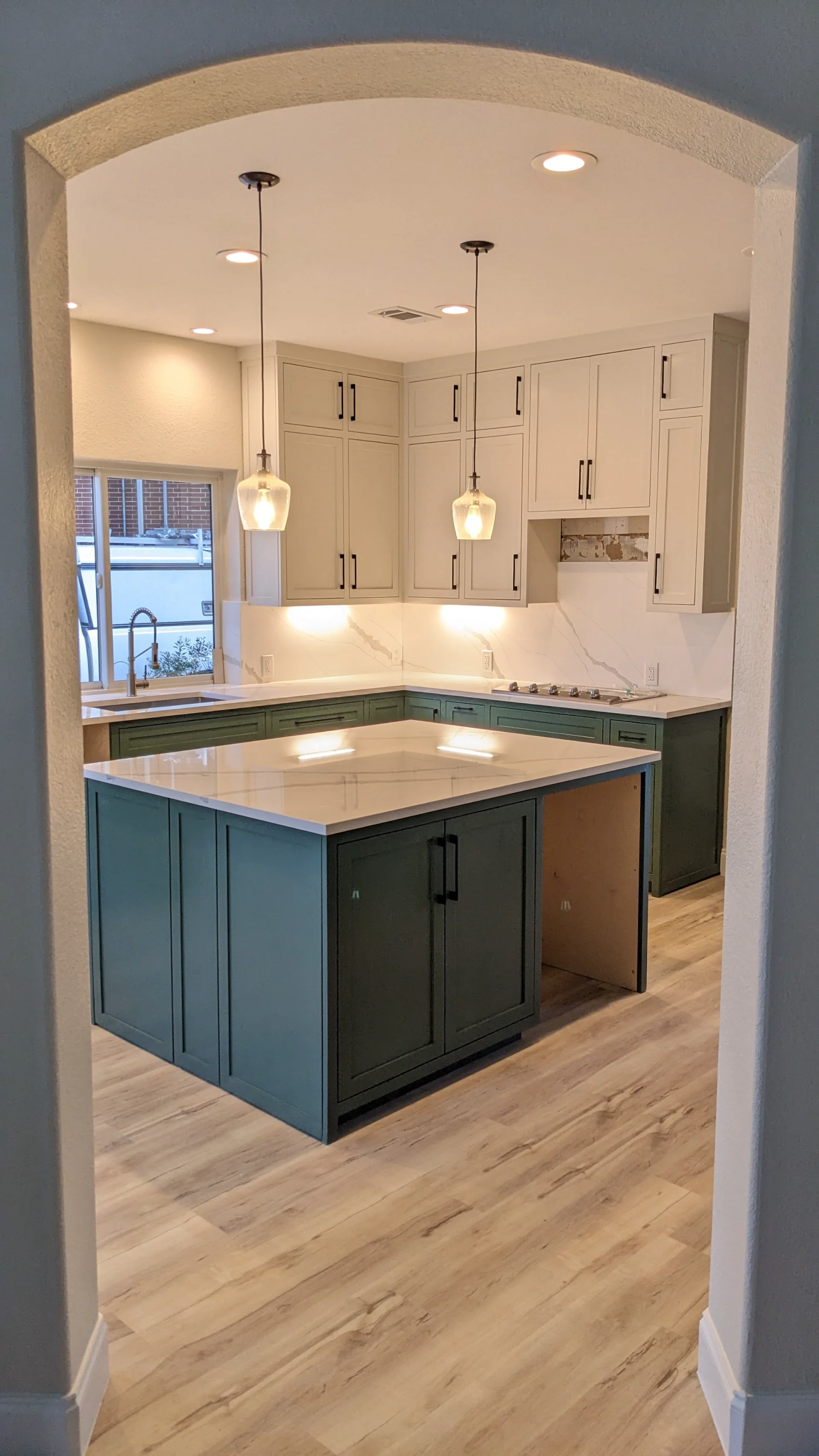 A modern two-tone kitchen remodel in Austin, Texas, showcasing off-white upper cabinets and deep teal lower cabinets with black hardware. The design features marble-patterned quartz countertops and backsplash, a central island, and recessed lighting in a Tarrytown home. - Detail 6