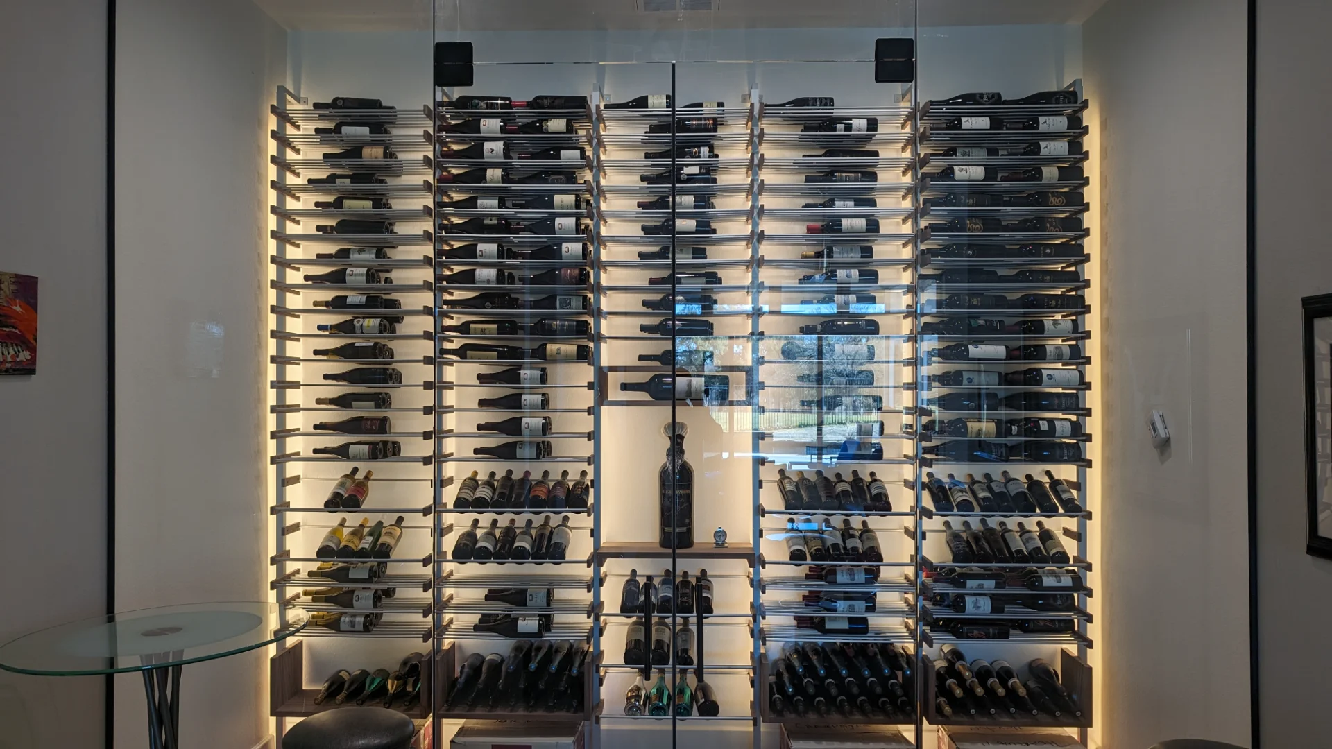 A sleek modern custom-built wine cellar featuring glass doors, horizontal metal shelving, and warm backlighting in a luxury residence located in the Texas Hill Country. - Detail 2