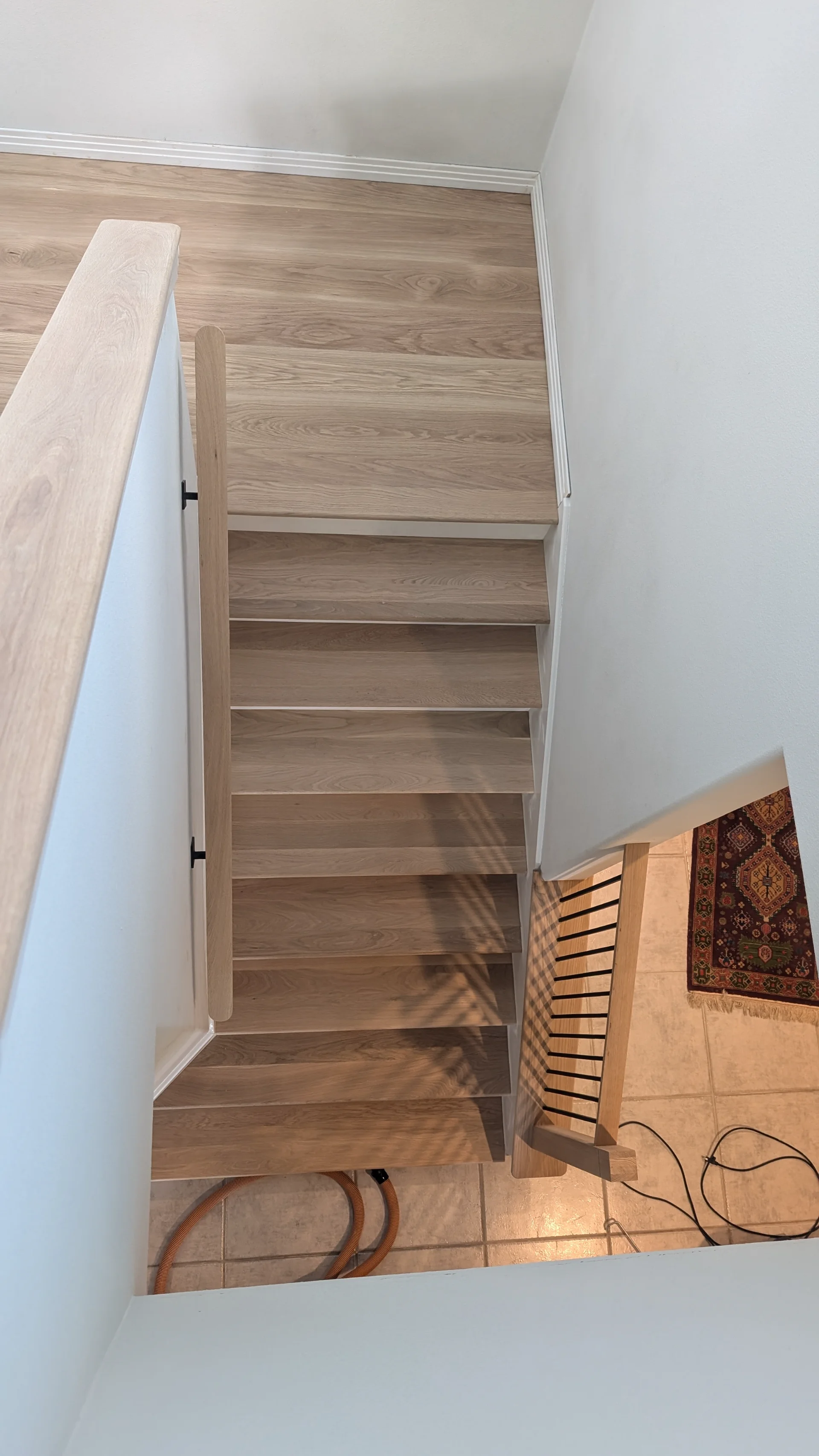 A modern residential staircase with light wood treads and white risers, featuring a contemporary railing with black metal balusters and a light wood handrail, perfectly suited for a home in Austin or West Lake Hills. - Detail 3