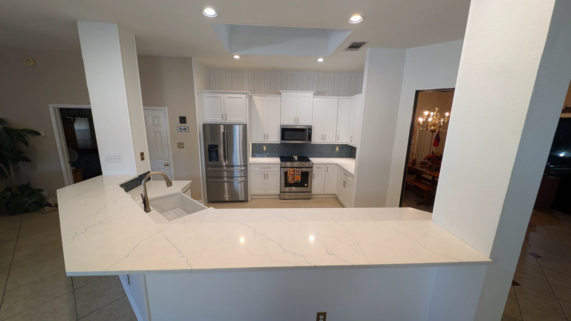 A modern kitchen remodel in Austin, Texas, featuring white shaker-style cabinetry with gold hardware, a blue-grey tile backsplash, white quartz countertops, and stainless steel KitchenAid appliances including a French door refrigerator and a slide-in range. - Detail 2