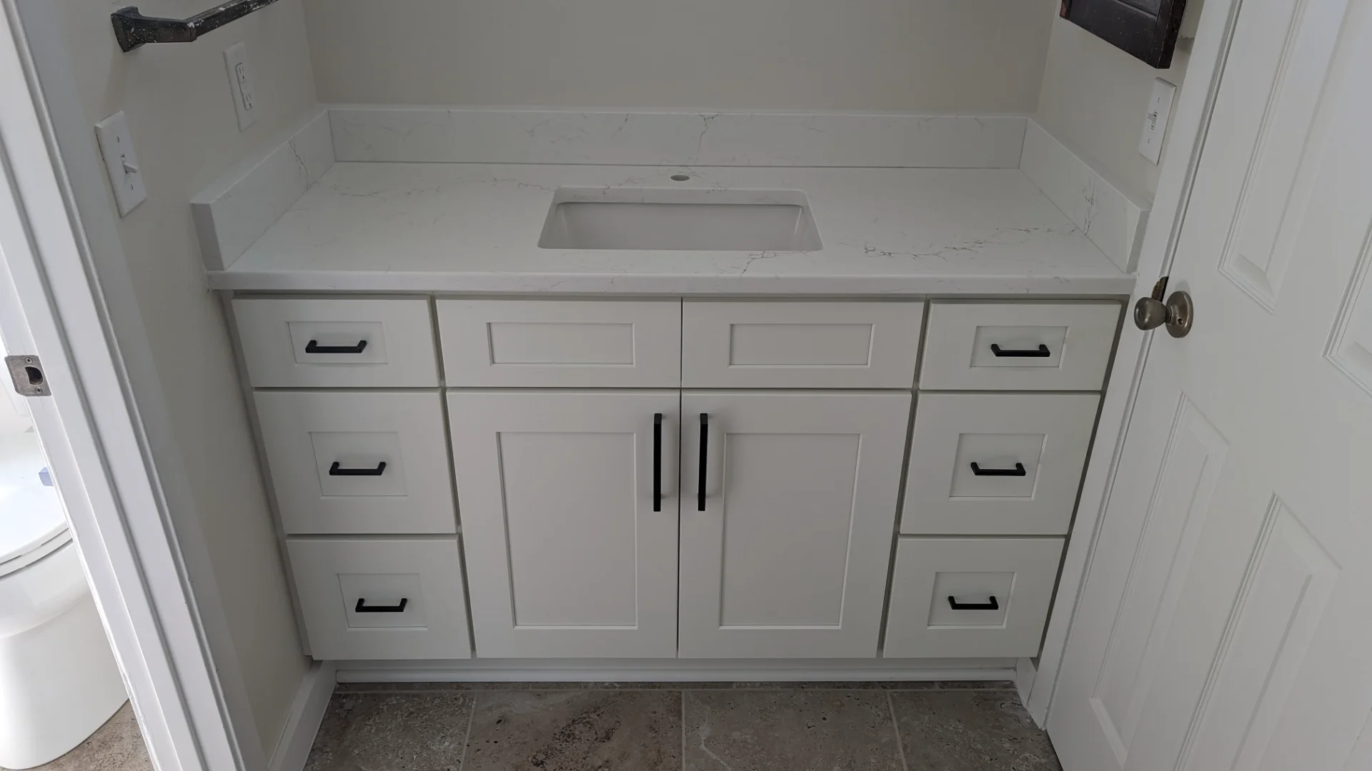 A newly renovated modern kitchen from a New Project in Austin, Texas, showcasing white shaker cabinets with black hardware, speckled brown granite countertops, and a large kitchen island. This bright, functional design is ideal for homes in West Lake Hills, Dripping Springs, Tarrytown, and the greater Texas Hill Country. - Detail 2