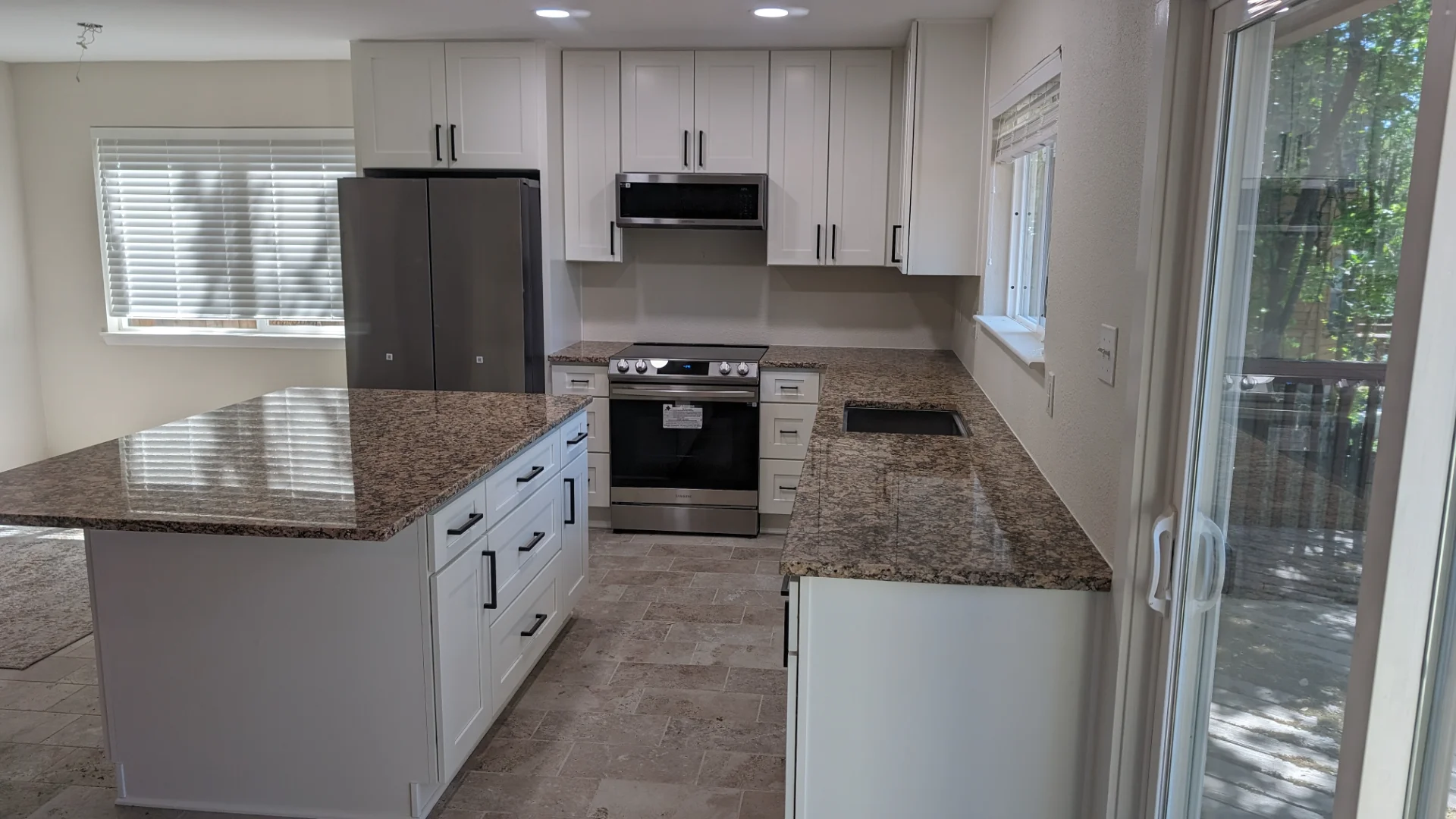 A newly renovated modern kitchen from a New Project in Austin, Texas, showcasing white shaker cabinets with black hardware, speckled brown granite countertops, and a large kitchen island. This bright, functional design is ideal for homes in West Lake Hills, Dripping Springs, Tarrytown, and the greater Texas Hill Country. - Detail 3