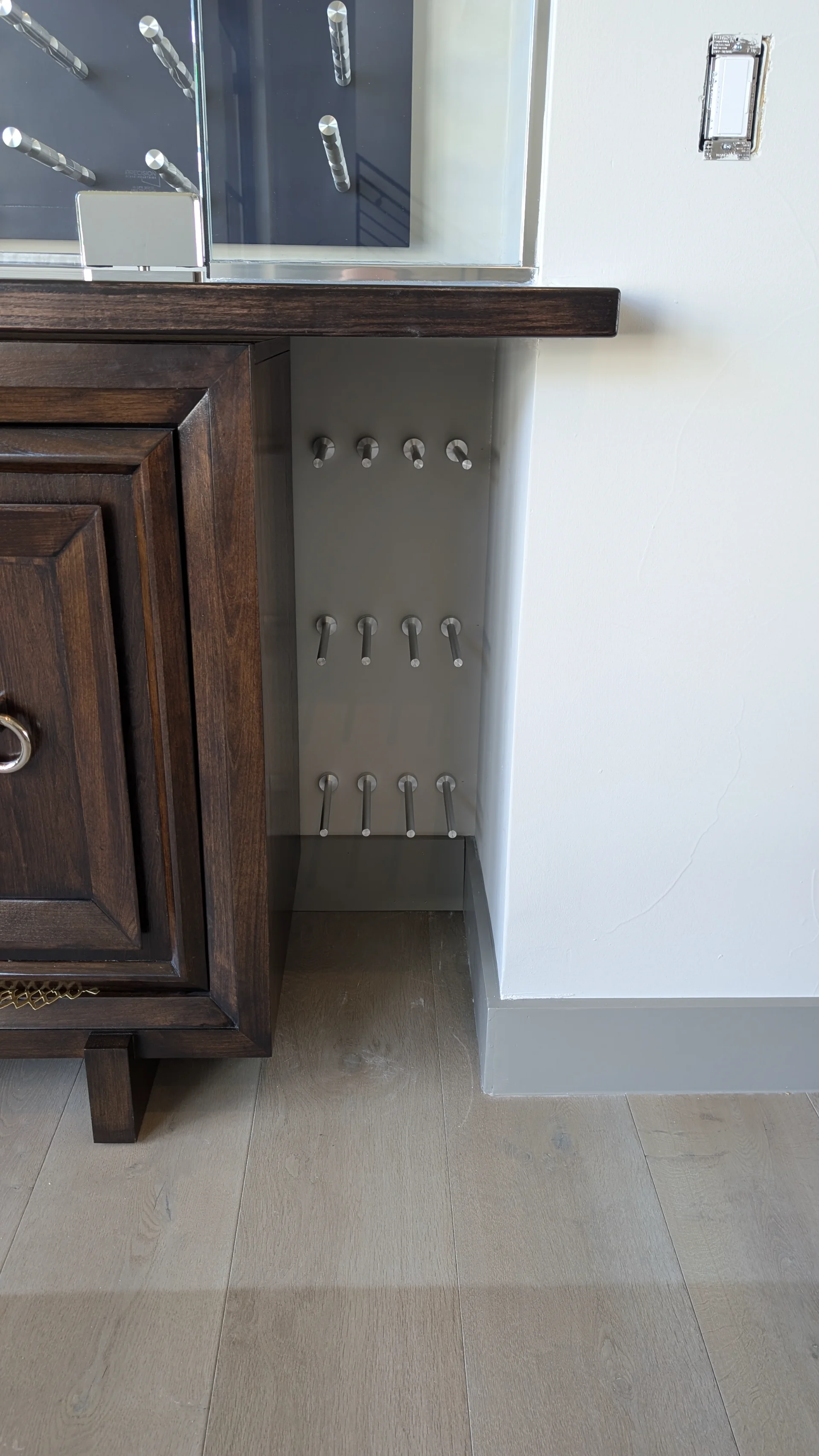 A modern, glass-enclosed wine cellar display with sleek chrome pegs against a dark navy background, set above a dark wood buffet cabinet in a luxury Austin, Texas home. - Detail 2
