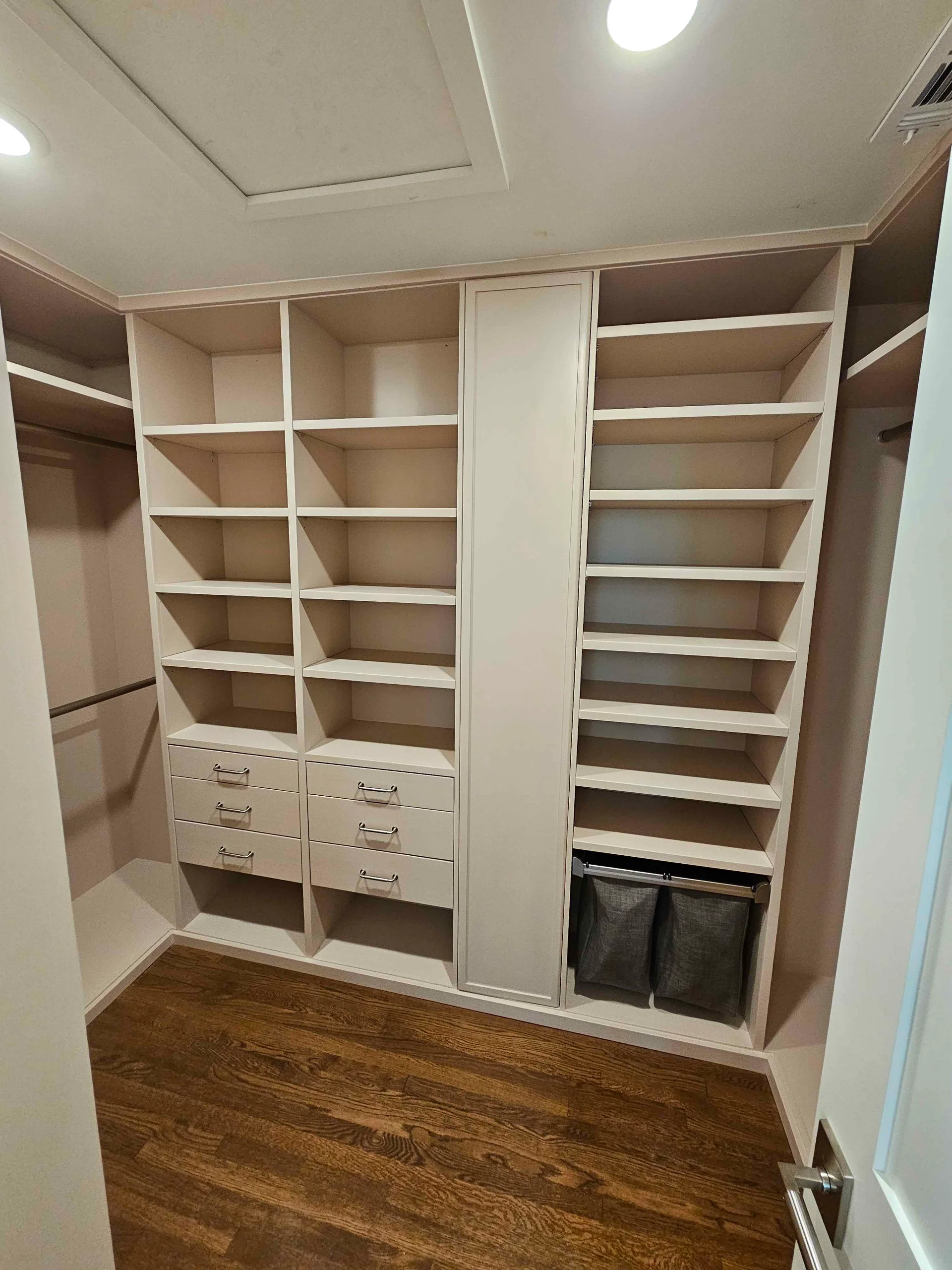 Spacious custom walk-in closet featuring floor-to-ceiling beige cabinetry with open shelving and integrated drawers, set against dark wood floors in a Tarrytown, Austin home. - Detail 3