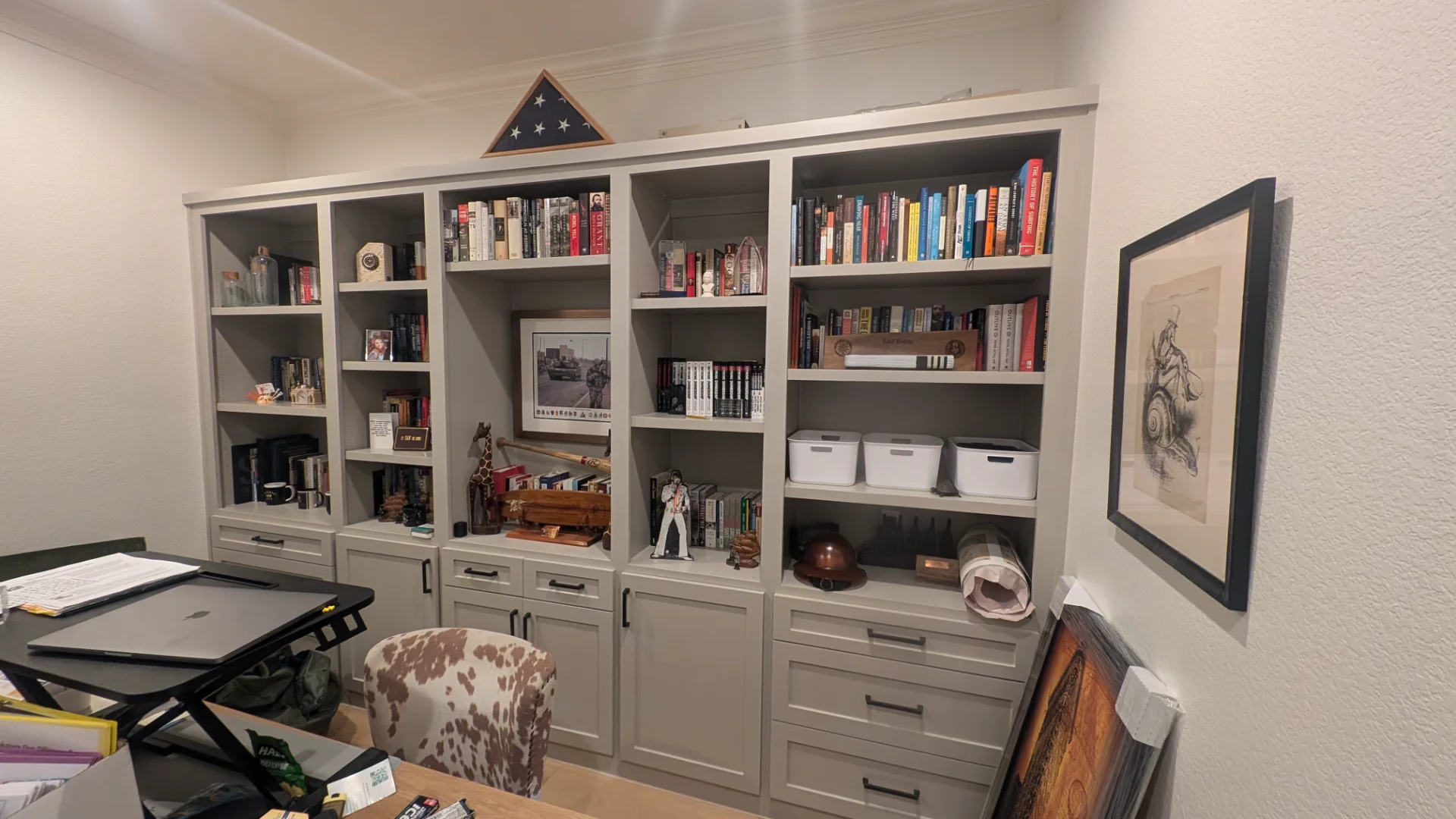 A custom-designed floor-to-ceiling light grey built-in shelving and cabinet unit in a home office, showcasing organized books, decorative items, and integrated storage in a West Lake Hills, Texas residence. - Detail 2