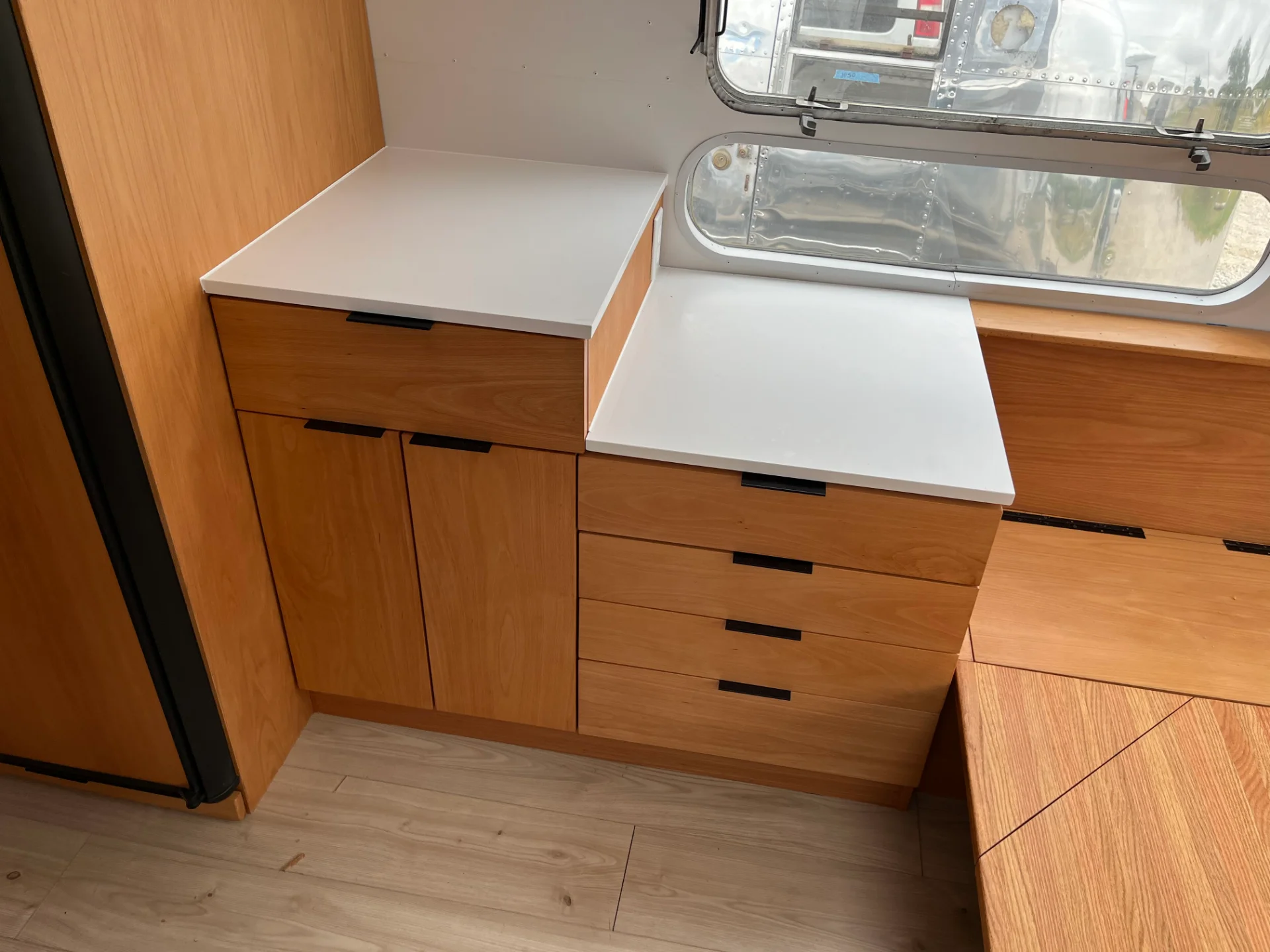 Modern interior of a renovated Airstream featuring custom light-wood cabinetry, a sleek black kitchenette, and wood-style flooring in a New Project located in Austin and the Texas Hill Country. - Detail 12