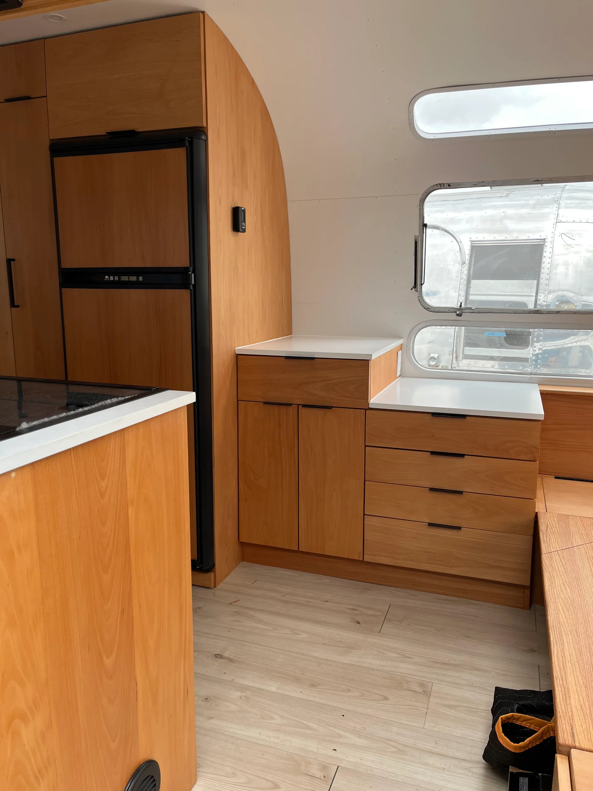 Modern interior of a renovated Airstream featuring custom light-wood cabinetry, a sleek black kitchenette, and wood-style flooring in a New Project located in Austin and the Texas Hill Country. - Detail 13
