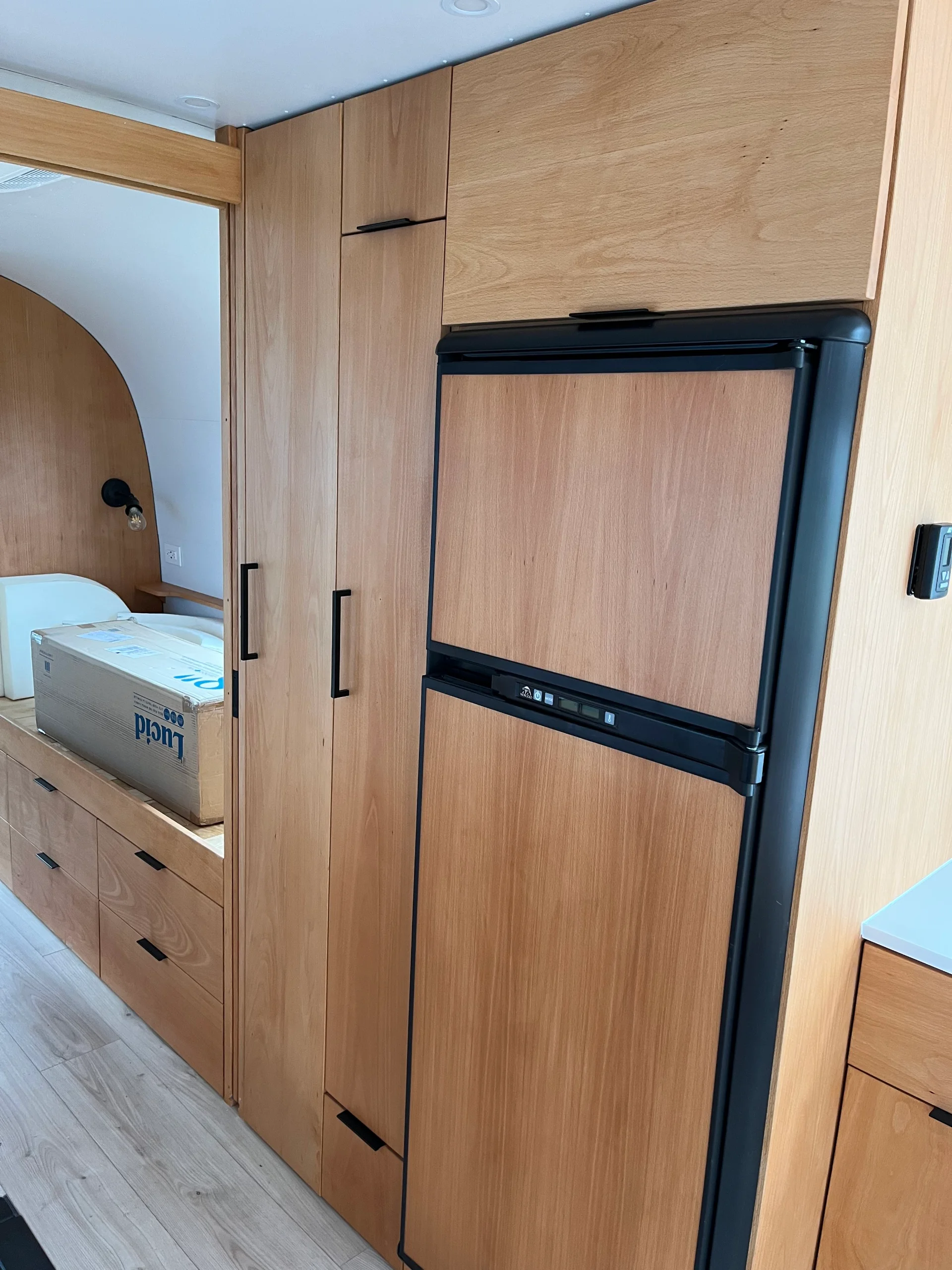 Modern interior of a renovated Airstream featuring custom light-wood cabinetry, a sleek black kitchenette, and wood-style flooring in a New Project located in Austin and the Texas Hill Country. - Detail 14