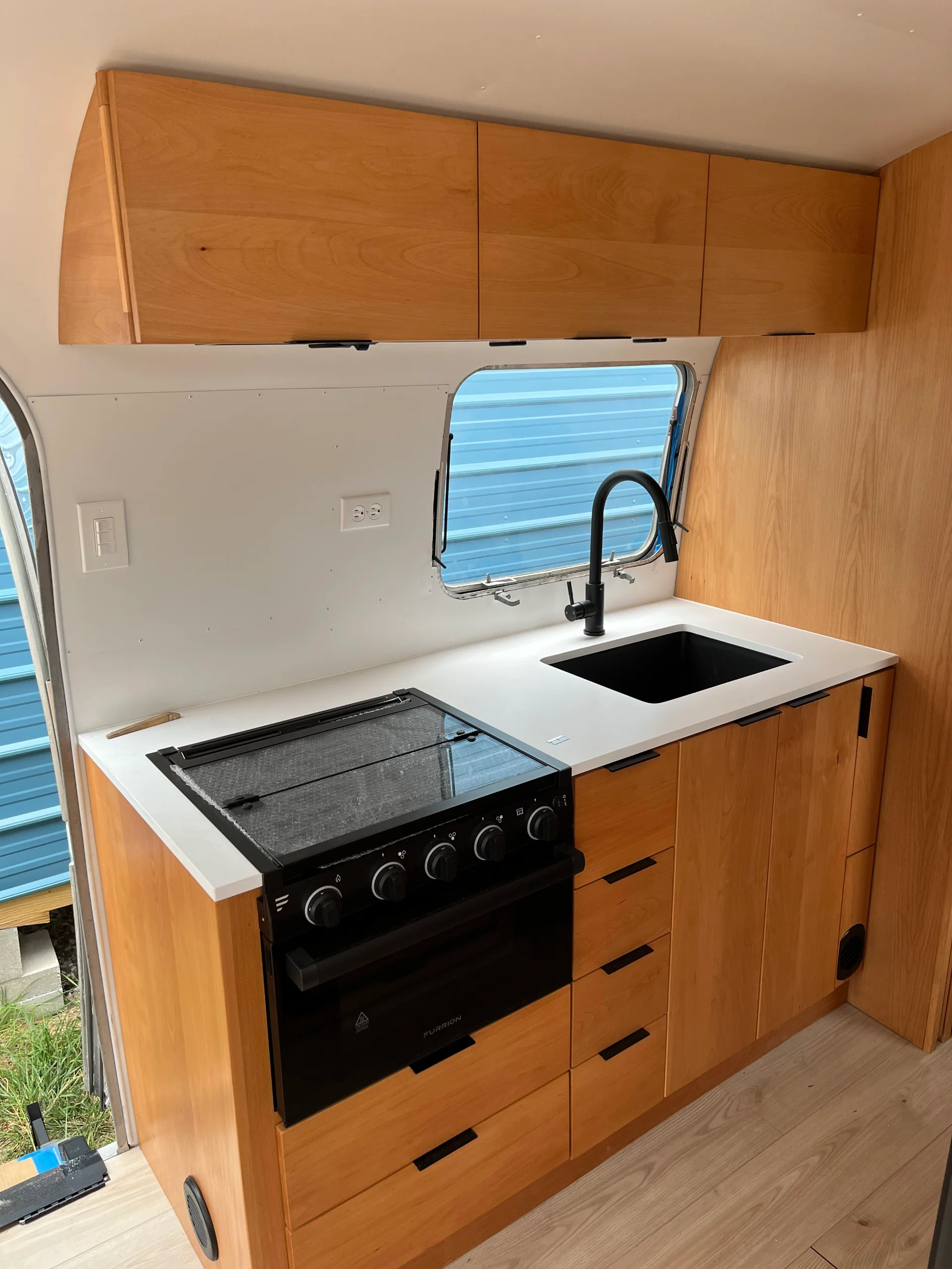 Modern interior of a renovated Airstream featuring custom light-wood cabinetry, a sleek black kitchenette, and wood-style flooring in a New Project located in Austin and the Texas Hill Country. - Detail 15