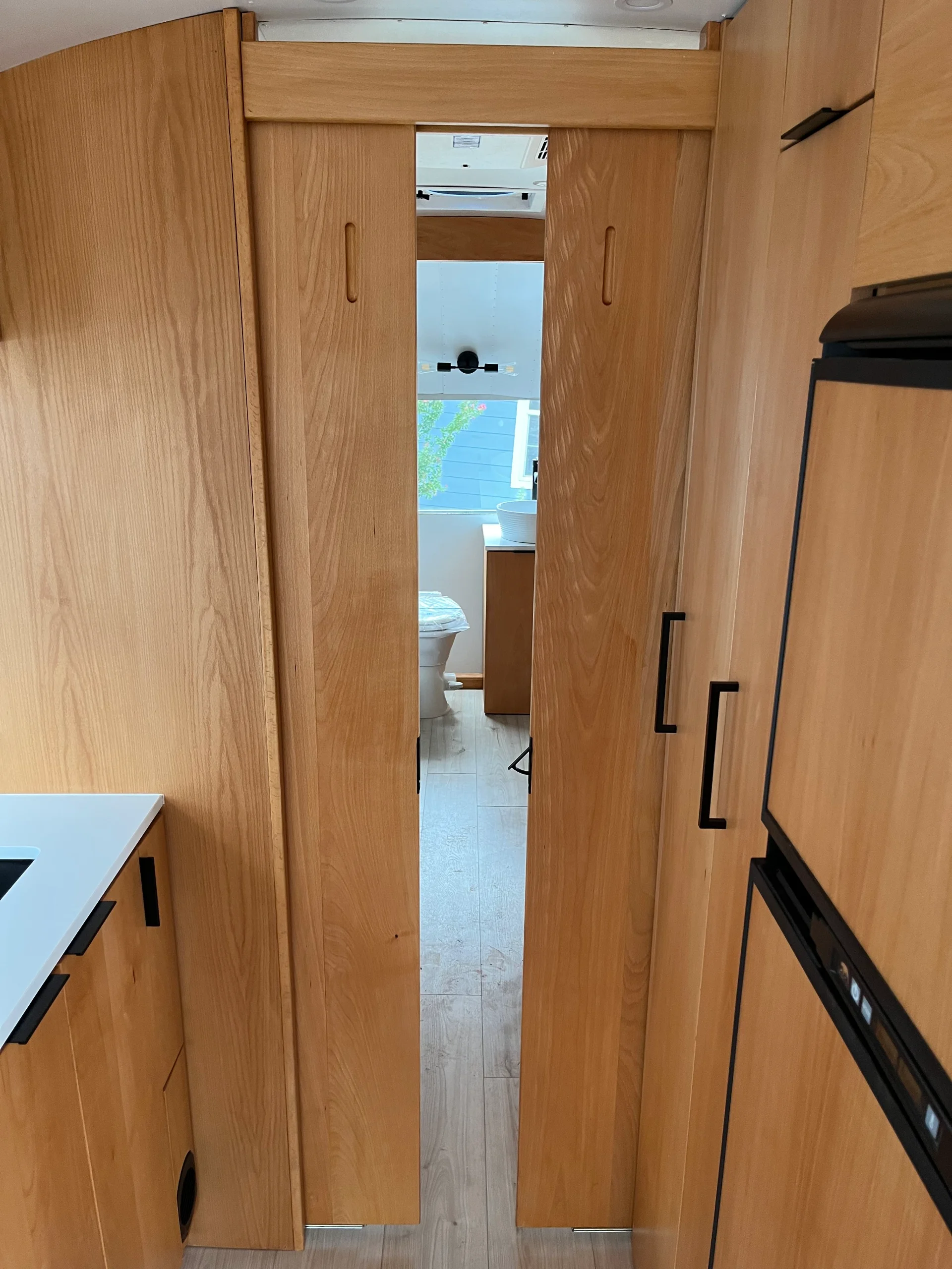 Modern interior of a renovated Airstream featuring custom light-wood cabinetry, a sleek black kitchenette, and wood-style flooring in a New Project located in Austin and the Texas Hill Country. - Detail 17