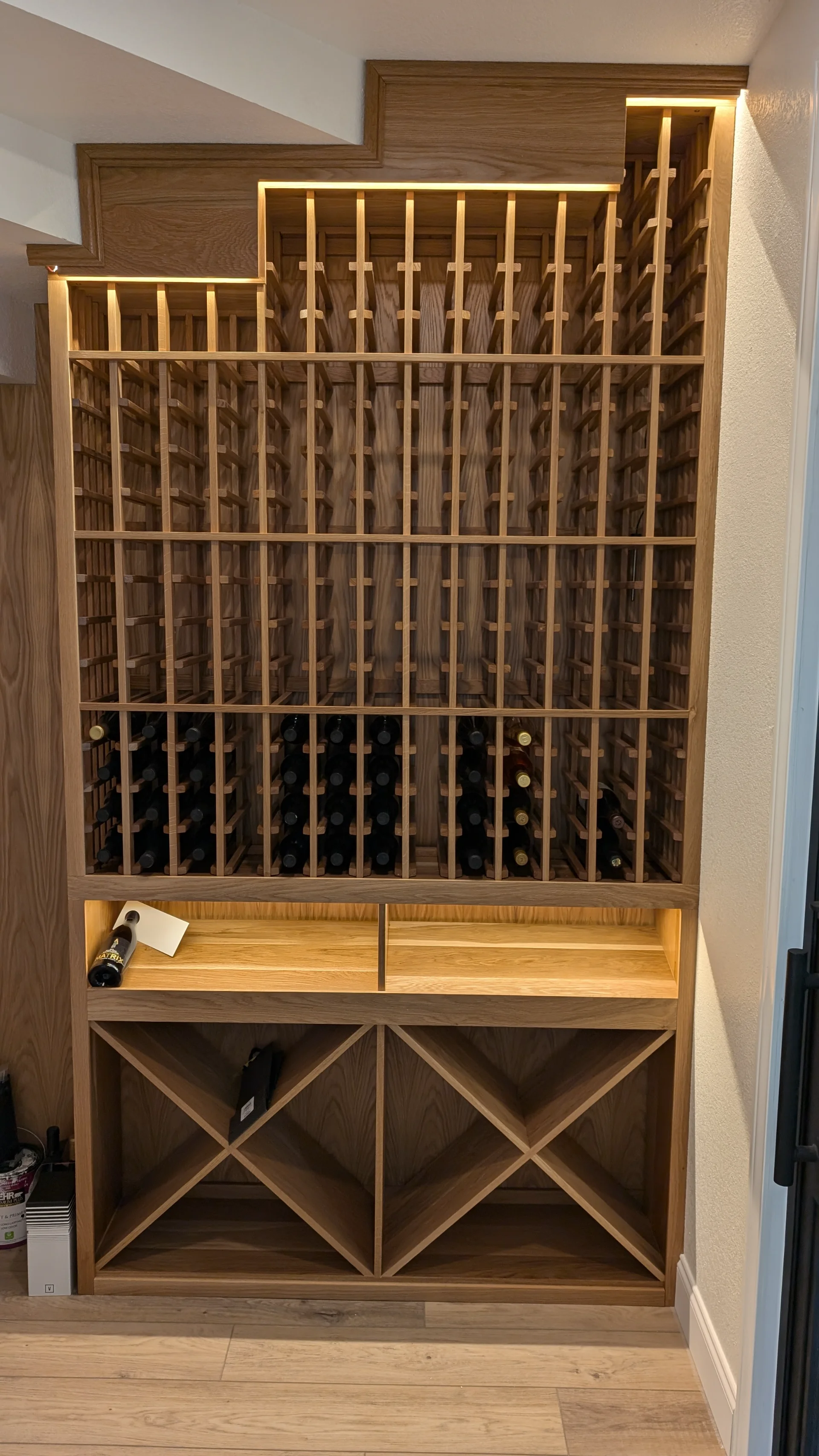Custom-built oak wine cellar from New Project, featuring integrated LED lighting, individual bottle slots, and diamond-shaped bulk storage bins in a home located in West Lake Hills, Texas. - Detail 1