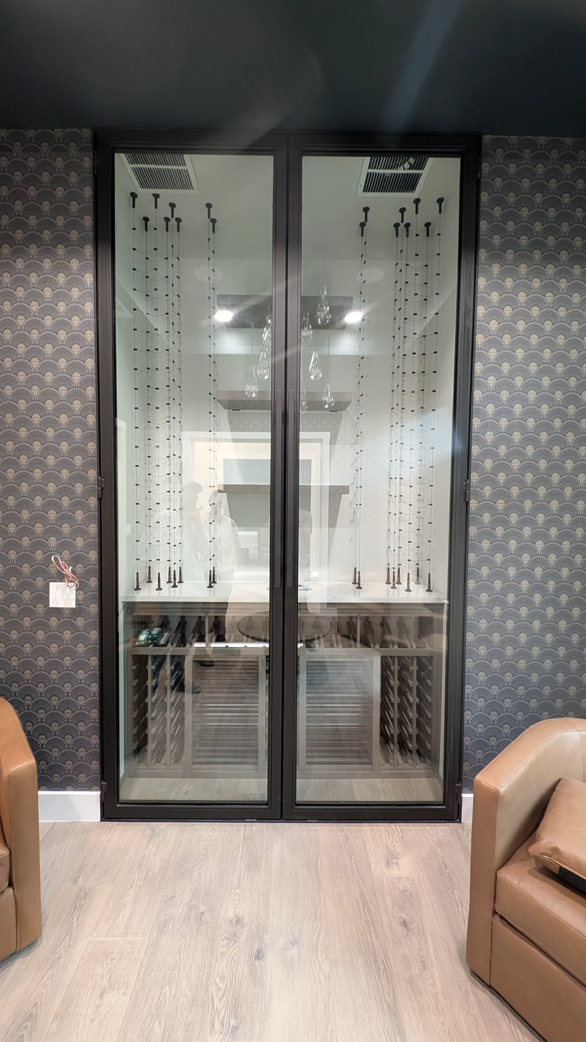 A luxury glass-enclosed wine cellar featuring custom wooden storage and cable wine racks, set against an Art Deco patterned wallpaper in a modern Austin, Texas home. - Detail 1
