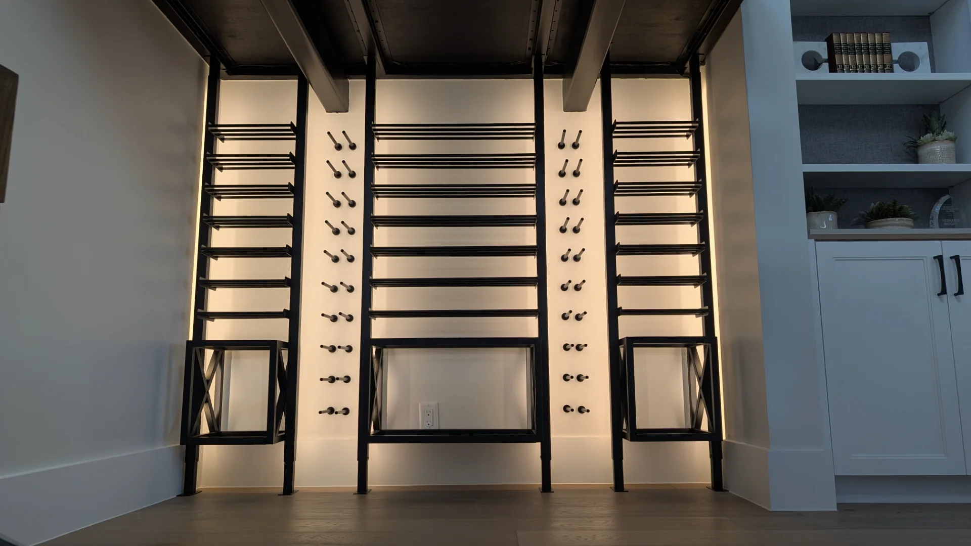A custom-designed modern black metal wine rack with sophisticated backlighting, installed in a luxury home bar area in Austin, featuring dark wood ceiling beams and sleek cabinetry. - Detail 1