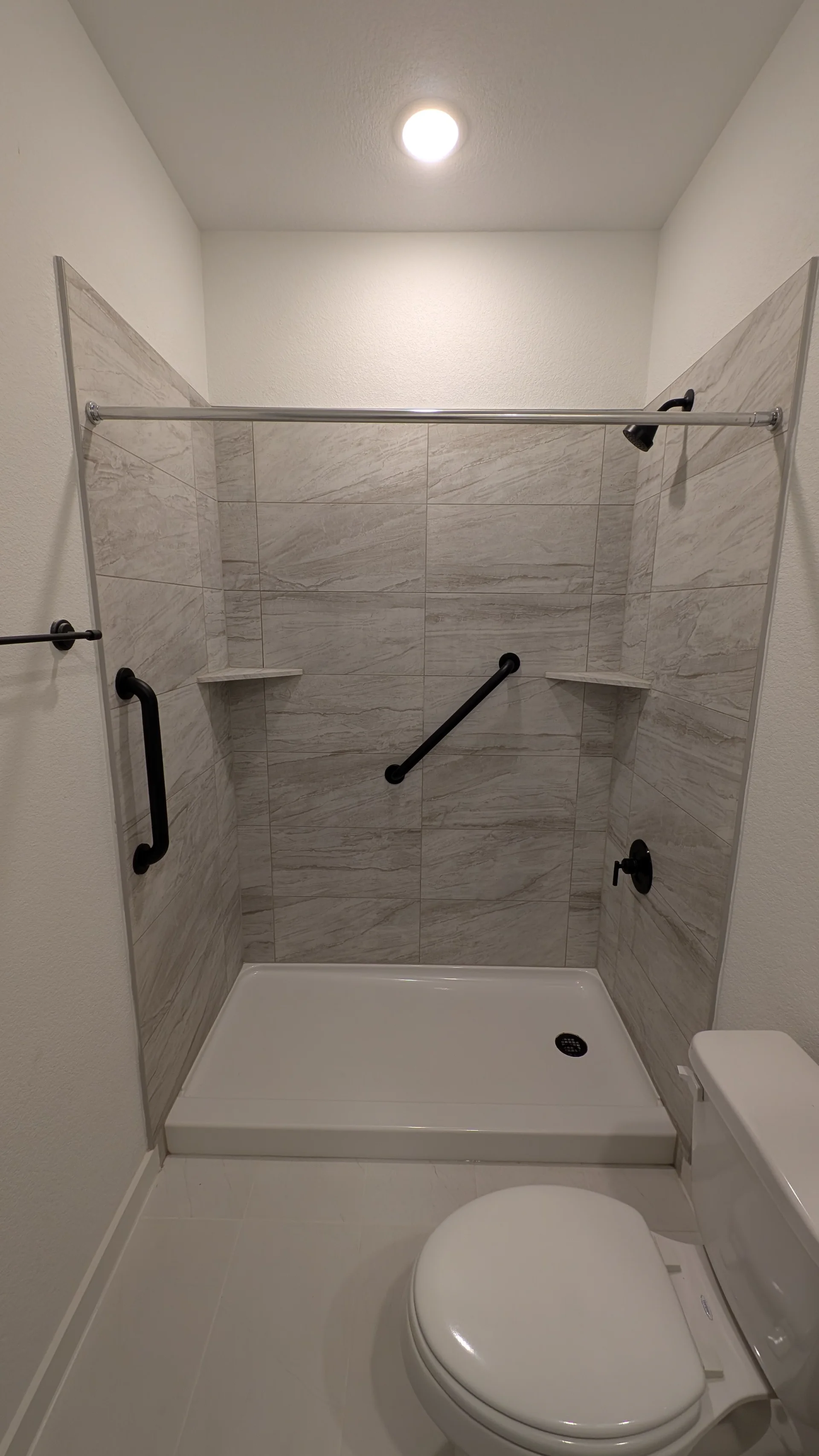 A modern walk-in shower featuring gray marble-look tile, matte black fixtures, and accessibility grab bars in a Tarrytown, Texas Hill Country home. - Detail 1