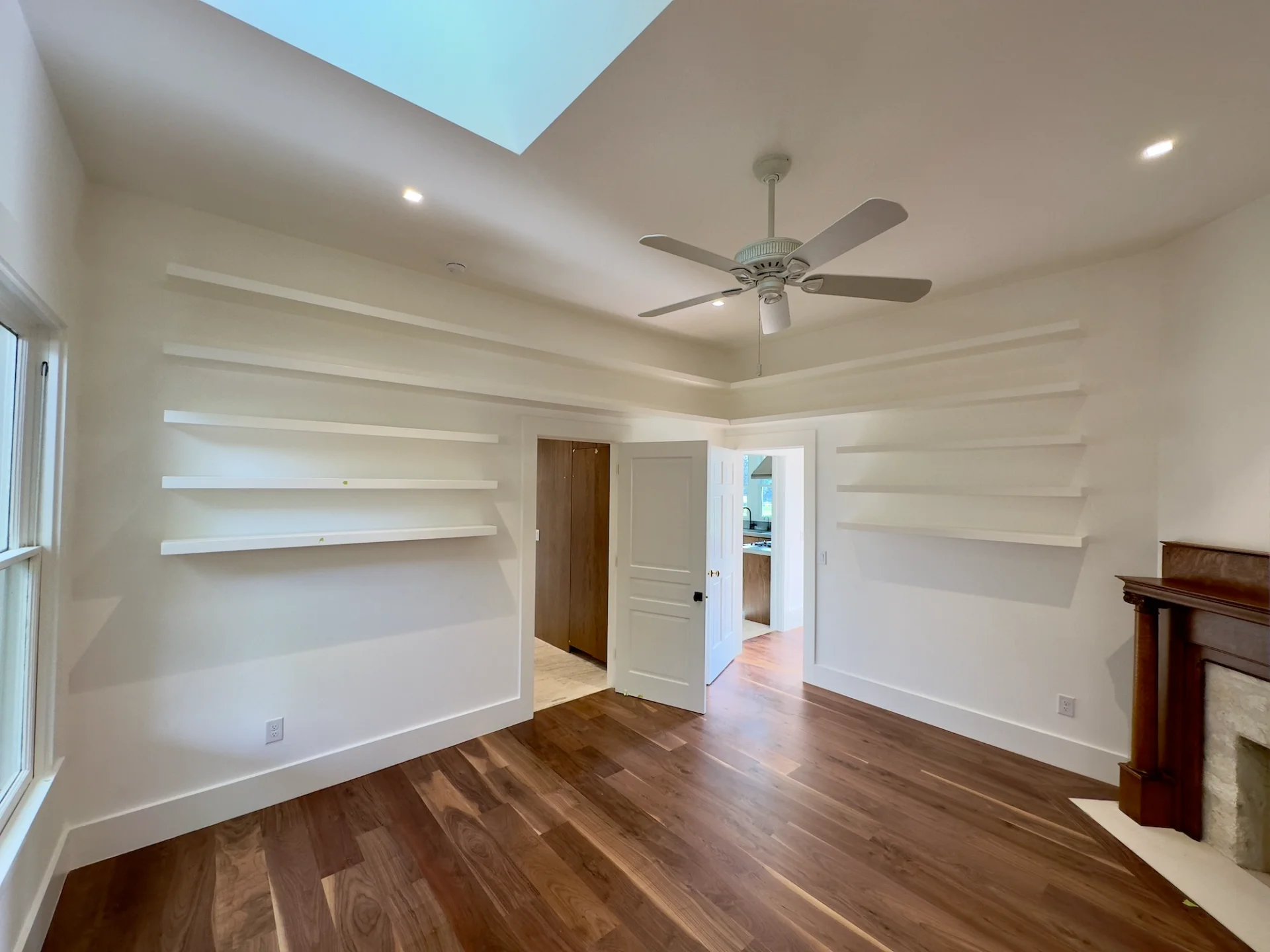 Modern custom home interior in West Lake Hills, Austin, featuring elegant hardwood floors, built-in floating shelves, a bright skylight, and a white ceiling fan. - Detail 1