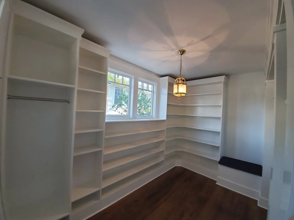 A luxurious custom walk-in closet with floor-to-ceiling white built-in shelving, a hanging rod, dark wood flooring, and a decorative gold lantern light fixture in an Austin, Texas Hill Country home. - Detail 1