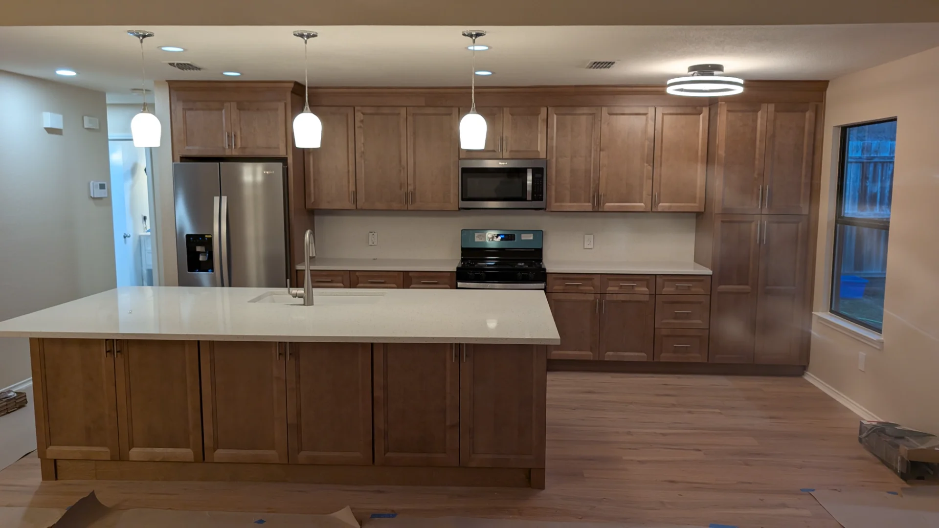 A newly completed modern kitchen remodel in Austin, Texas, featuring custom wood shaker cabinets, a large white quartz waterfall island with a sink, and stainless steel appliances. - Detail 1