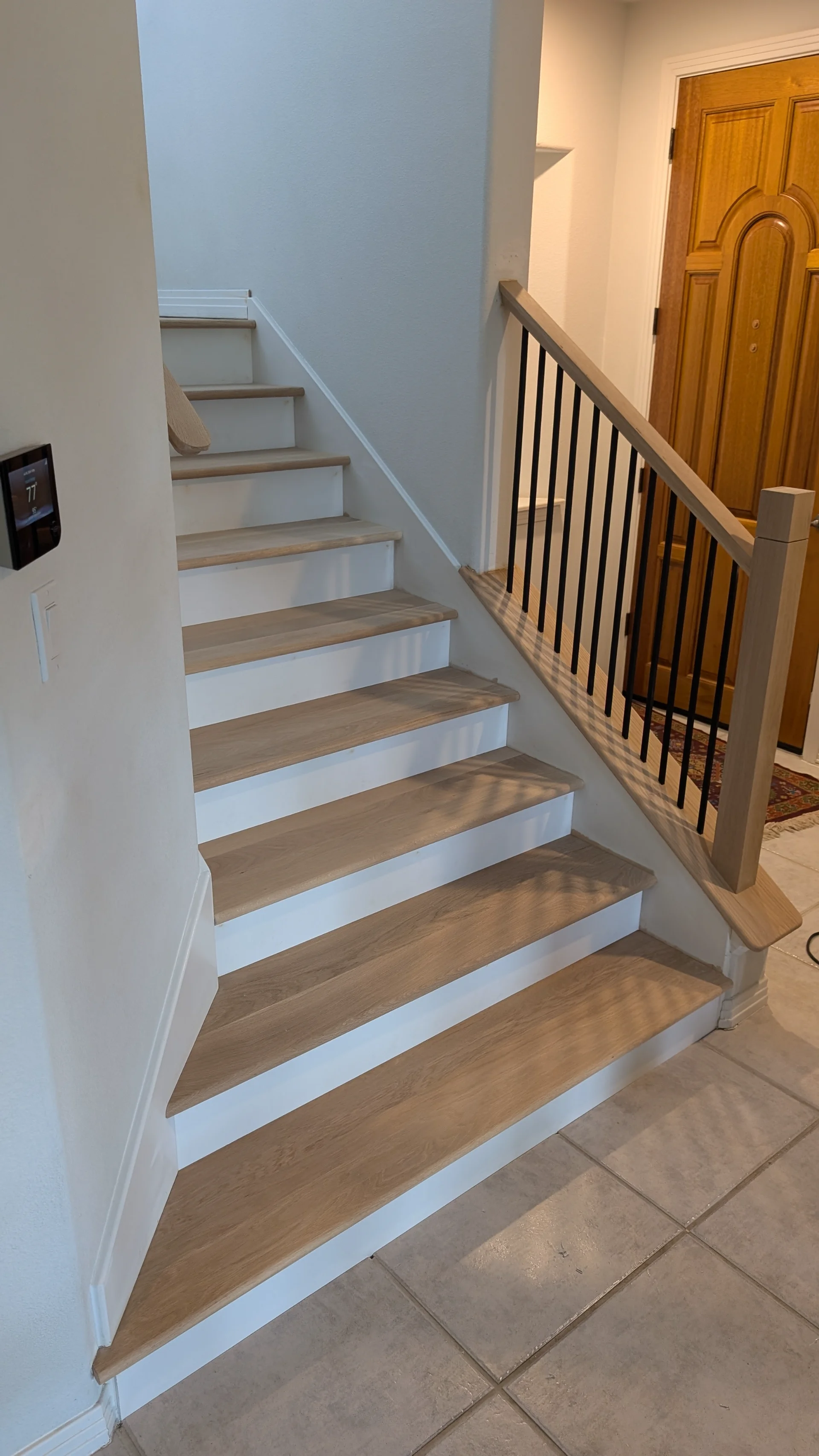 A modern residential staircase with light wood treads and white risers, featuring a contemporary railing with black metal balusters and a light wood handrail, perfectly suited for a home in Austin or West Lake Hills. - Detail 1
