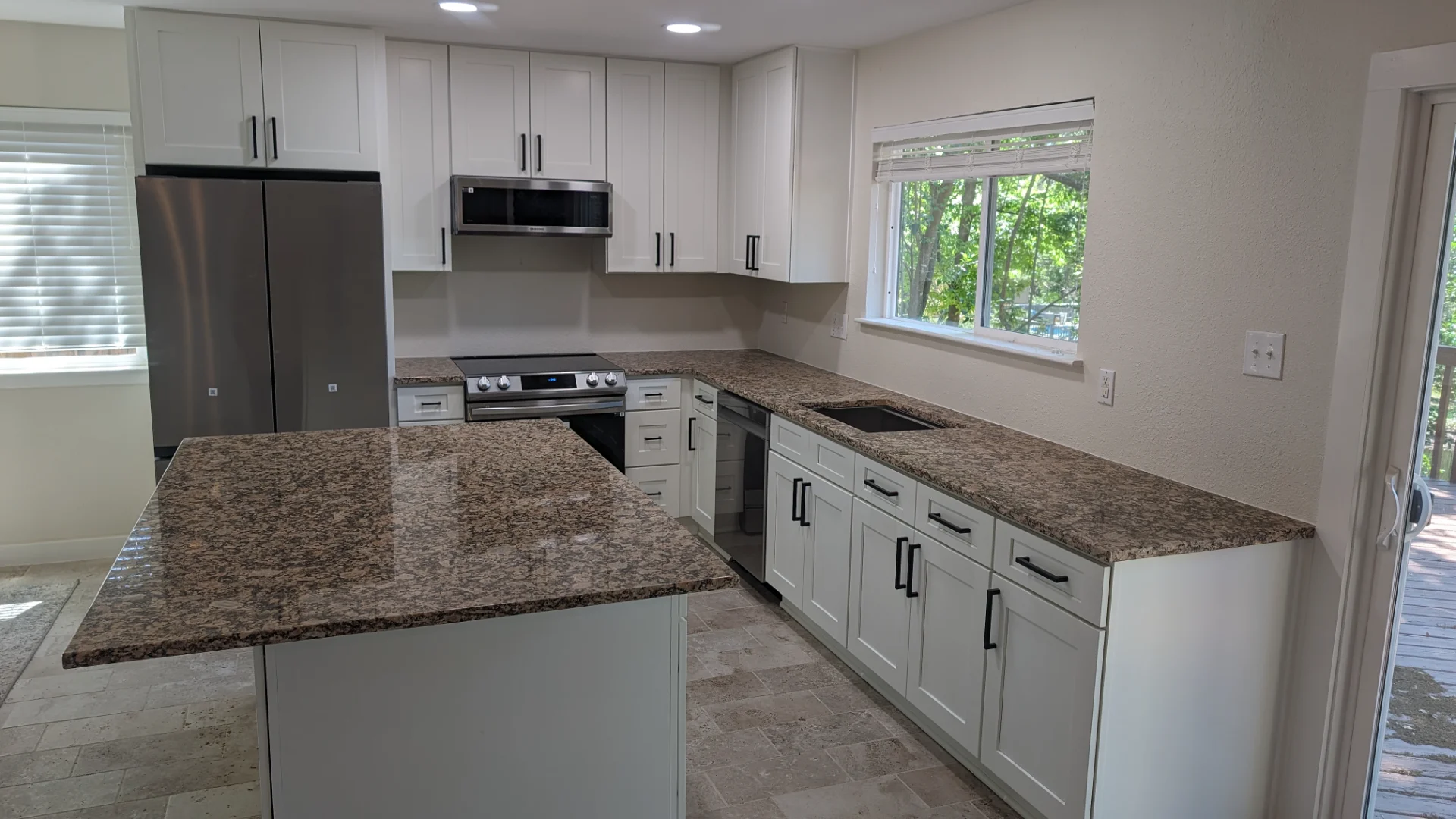 A newly renovated modern kitchen from a New Project in Austin, Texas, showcasing white shaker cabinets with black hardware, speckled brown granite countertops, and a large kitchen island. This bright, functional design is ideal for homes in West Lake Hills, Dripping Springs, Tarrytown, and the greater Texas Hill Country. - Detail 1