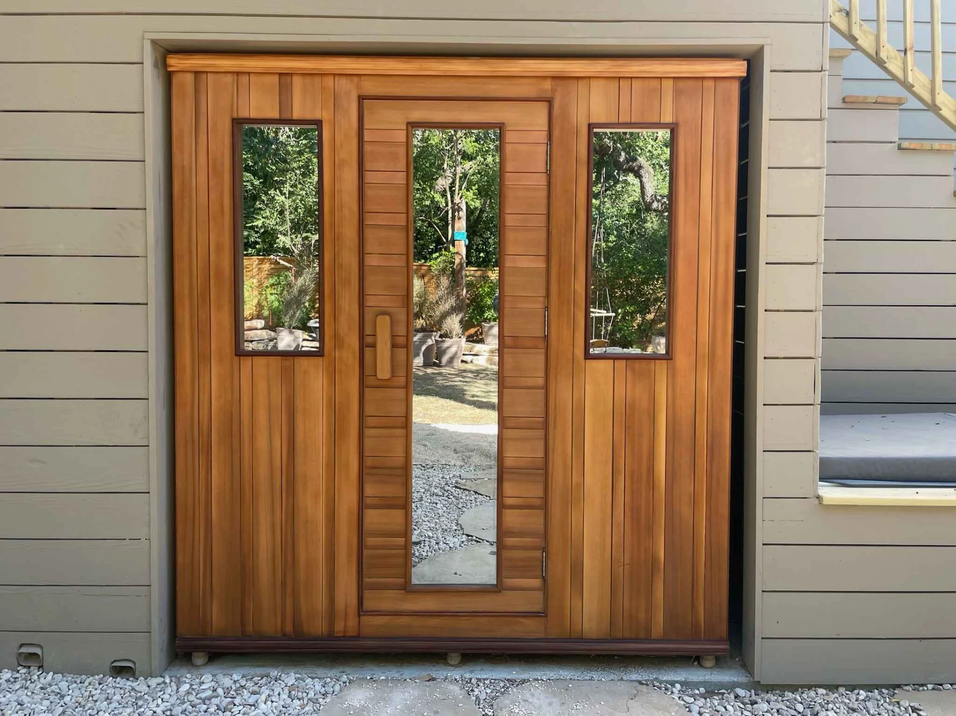 A modern outdoor sauna constructed from warm-toned wood, featuring a central door and two side panels with vertical windows, integrated into the architecture of a home in West Lake Hills, Austin. - Detail 1