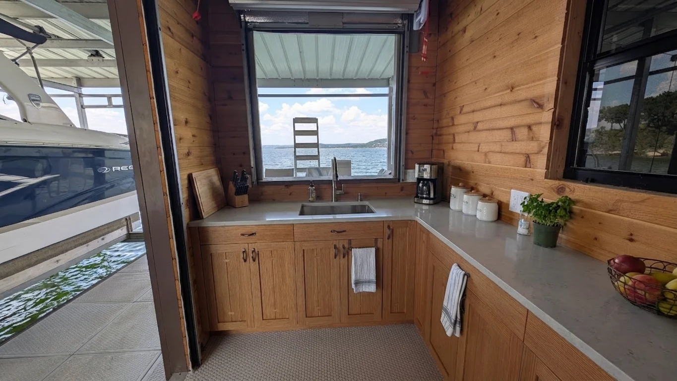 Interior view of a luxury artisan oak boat dock storage suite in West Lake Hills, Texas, featuring custom craftsman cabinetry, quartz countertops, and a scenic lakefront window next to a docked boat. - Detail 1