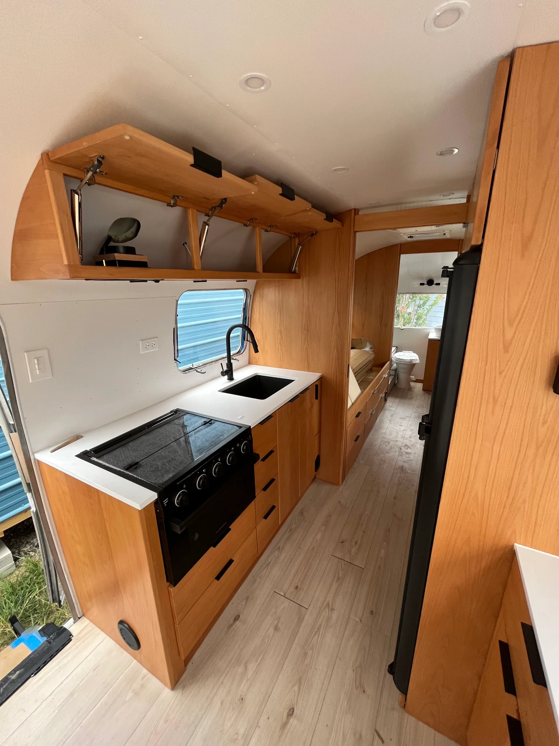 Modern interior of a renovated Airstream featuring custom light-wood cabinetry, a sleek black kitchenette, and wood-style flooring in a New Project located in Austin and the Texas Hill Country. - Detail 1