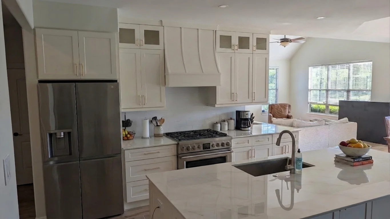 Transitional kitchen design in a Driftwood, Texas home featuring custom off-white cabinetry with gold hardware, a curved range hood, and white marble-look quartz countertops, serving homeowners in Austin and the Texas Hill Country.