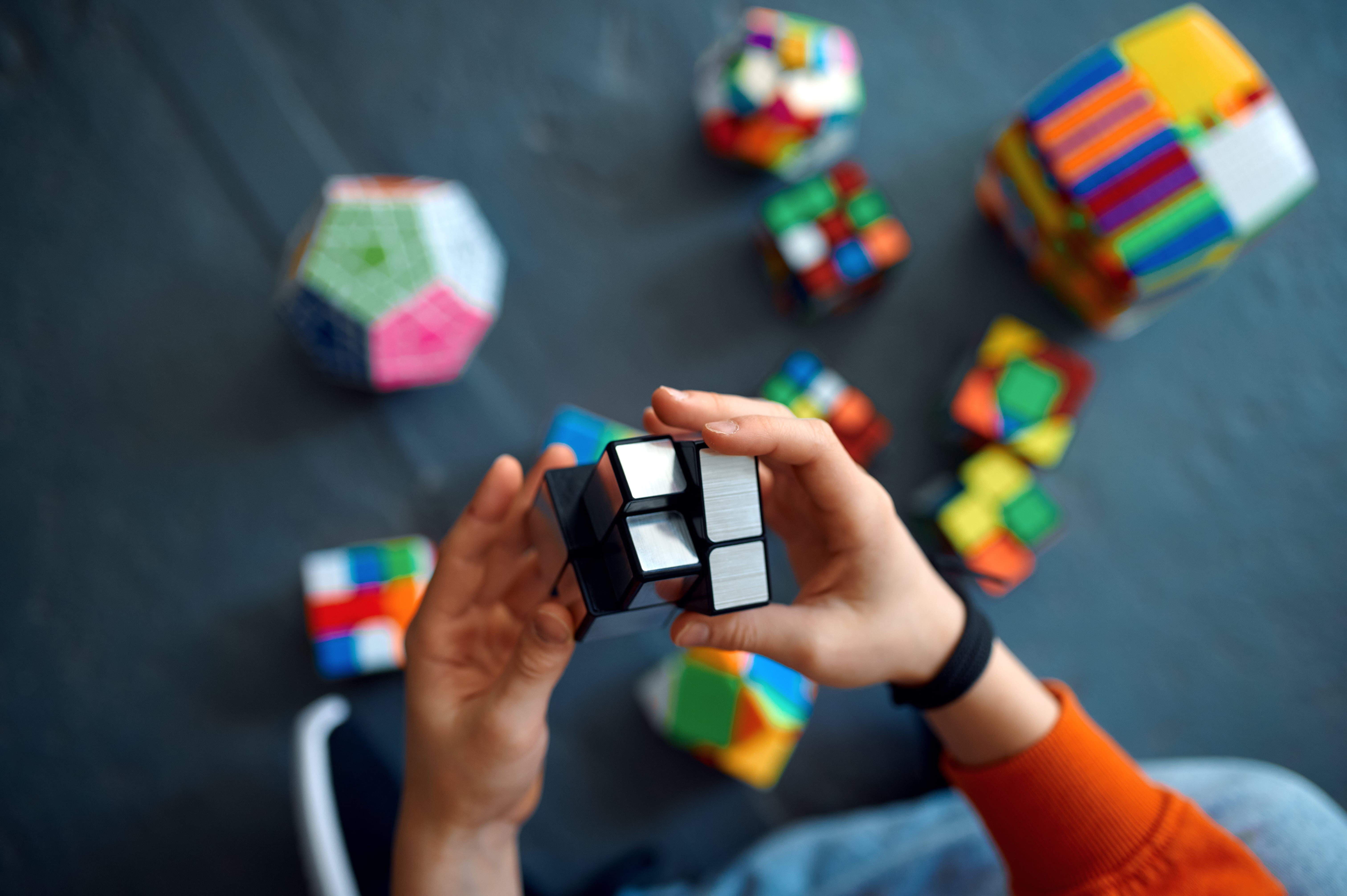 Closeup of hands playing with Rubik's Cube, other Rubik's cubes on the ground in background