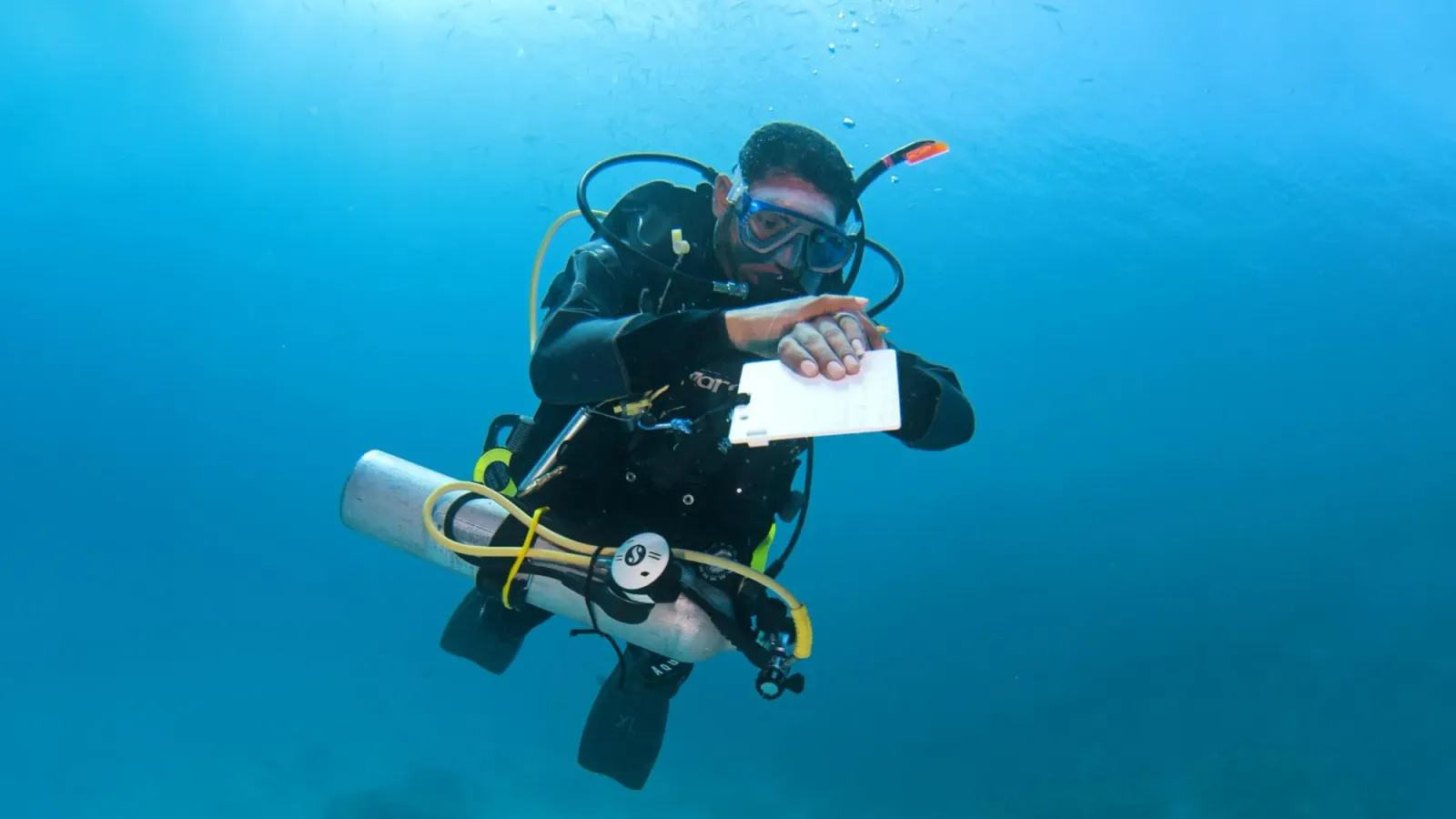 Taucher mit zusätzlicher Notflasche notiert etwas auf einer Schreibtafel im Freiwasser.