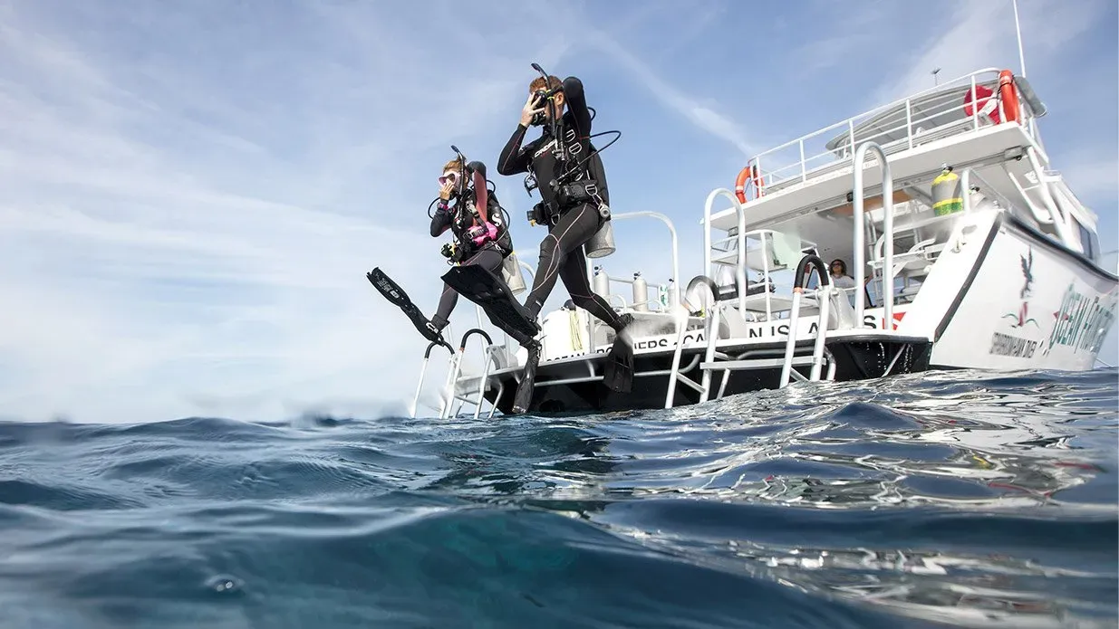 Zwei Taucher springen von der Plattform eines Tauchboots ins Meer.