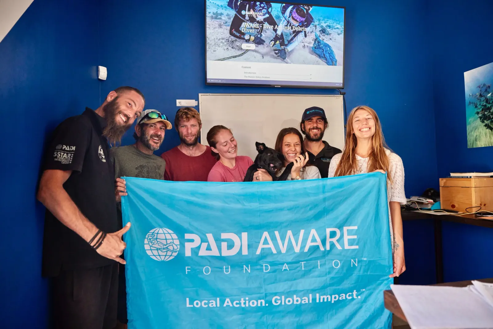 Gruppe von Menschen hält eine Fahne der PADI AWARE Foundation, im Hintergrund ein Kursbildschirm.