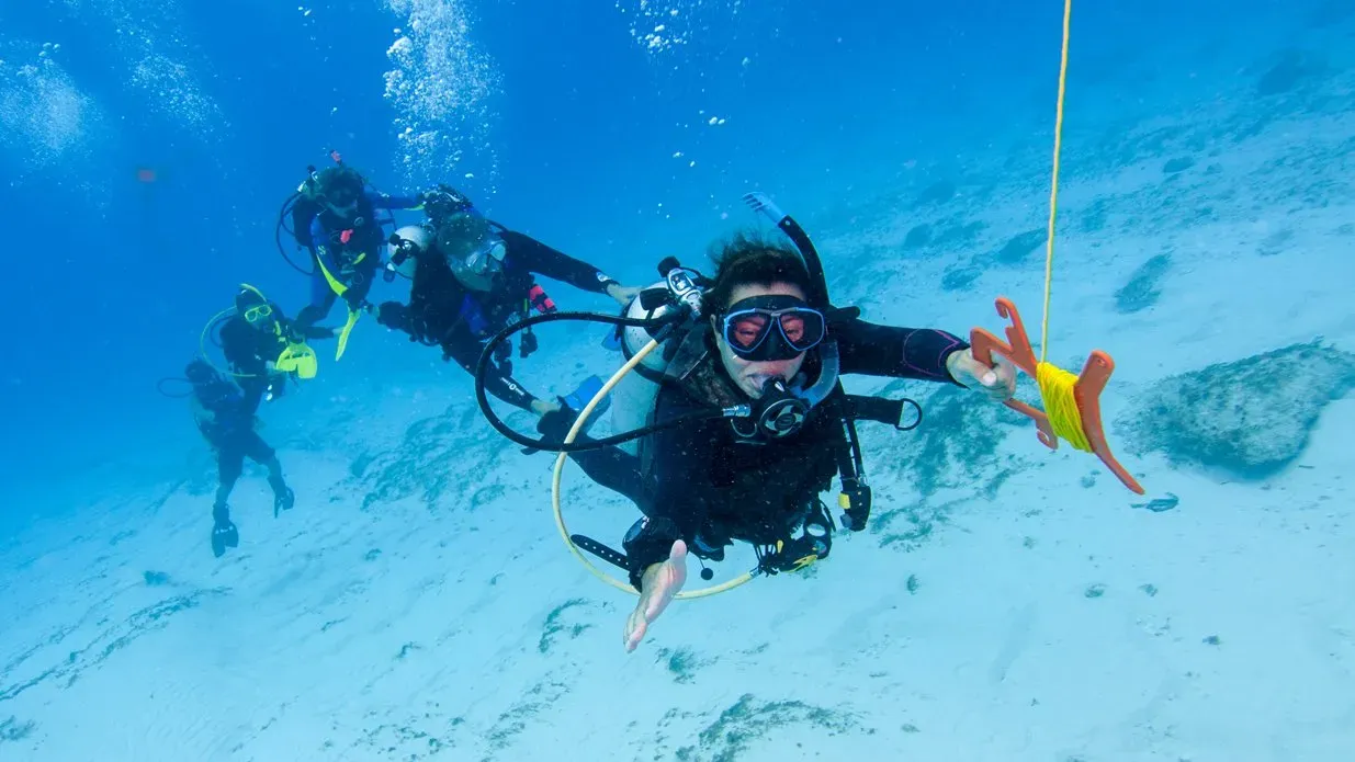 Tauchgruppe driftet über hellen Sandgrund, eine Taucherin lässt eine Signalboje aufsteigen.