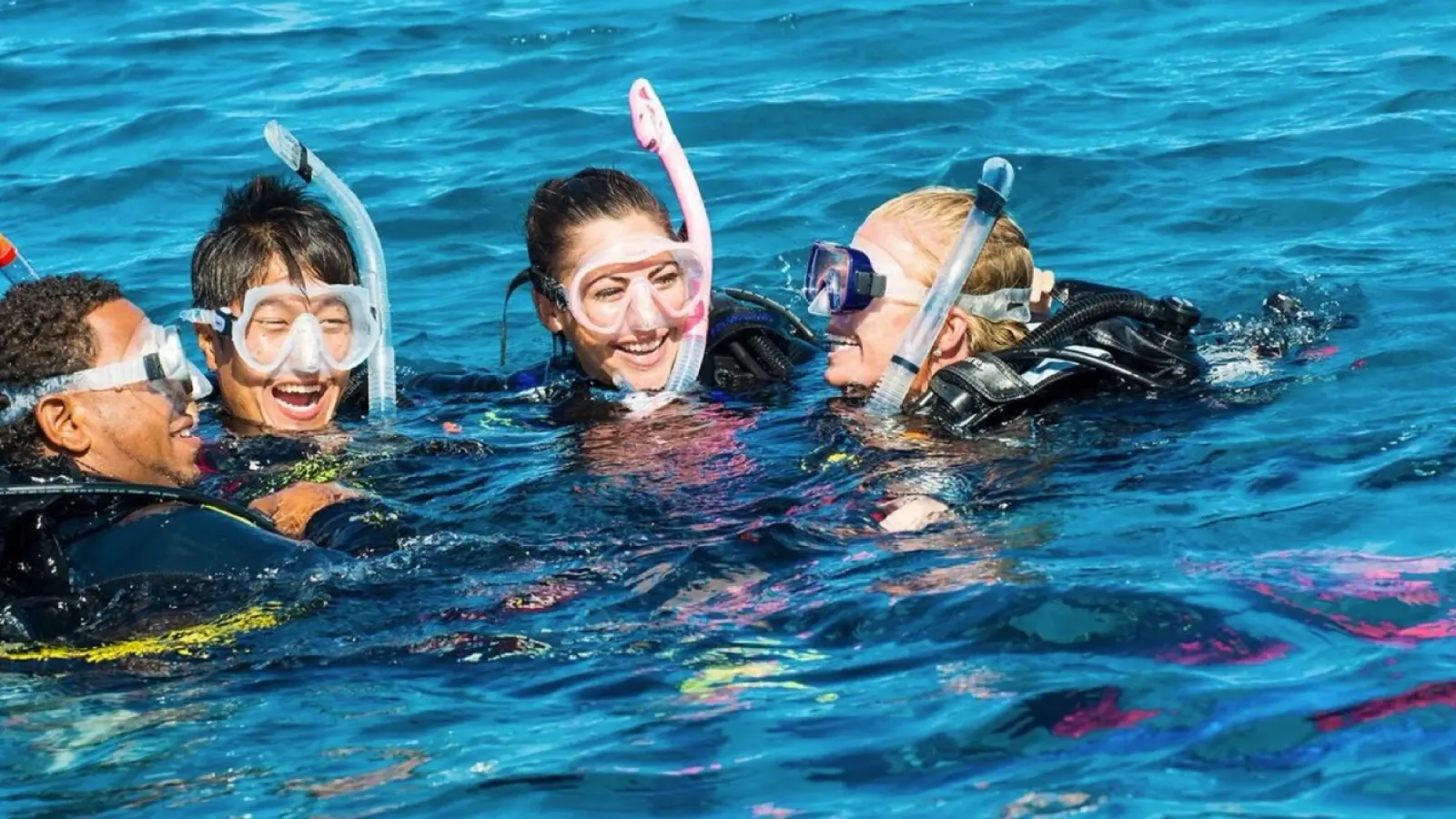 Vier lachende Menschen mit Maske und Schnorchel treiben nebeneinander an der Wasseroberfläche.