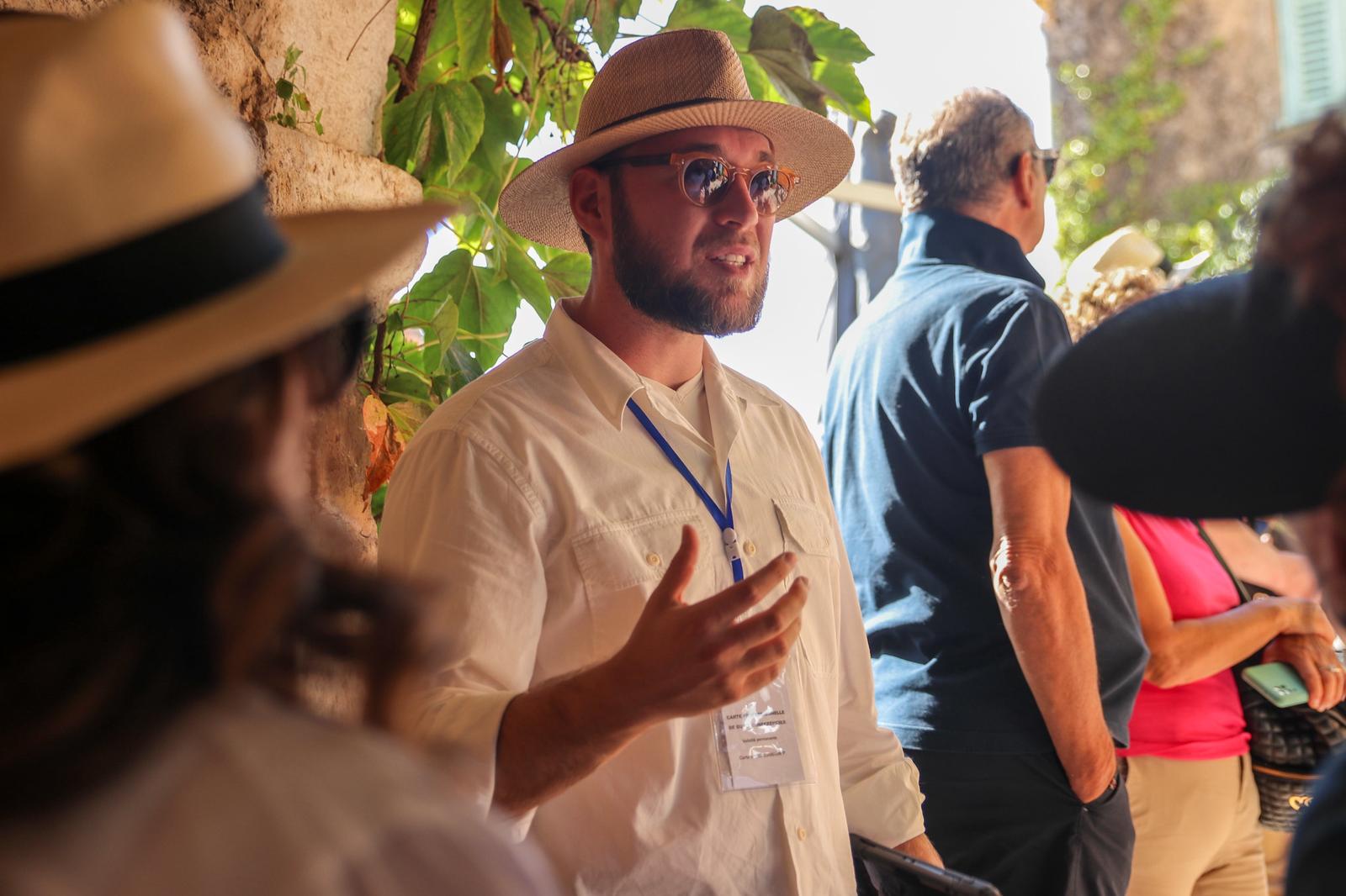 Magomed, a licensed tour guide wearing a white shirt, straw hat, and badge, speaking to visitors during the Eze and Monaco half-day tour.