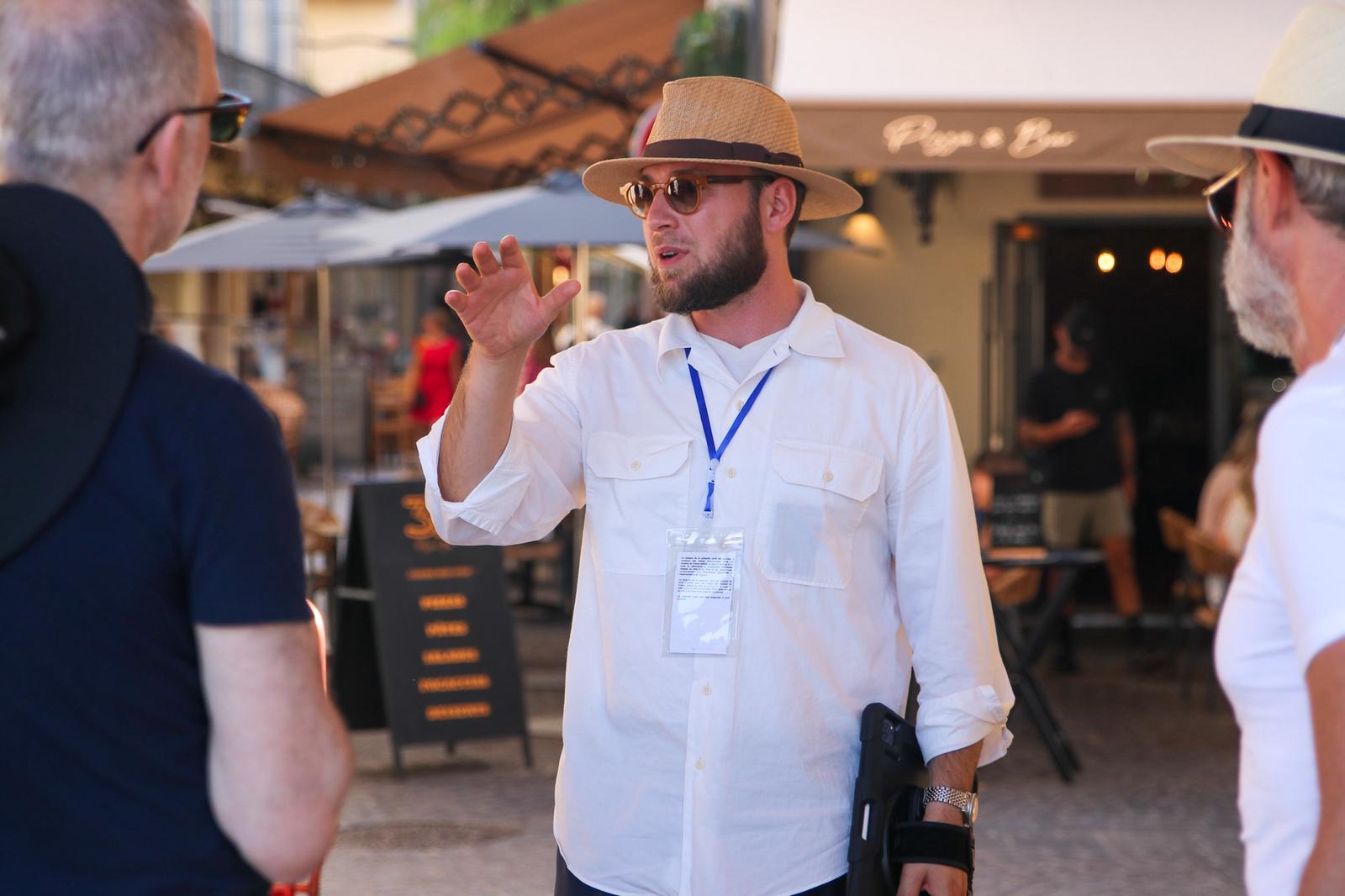 Magomed, a licensed tour guide wearing a white shirt, straw hat, and badge, explaining a point of interest to a small group during the full-day Cannes – Antibes – Saint-Paul-de-Vence tour.