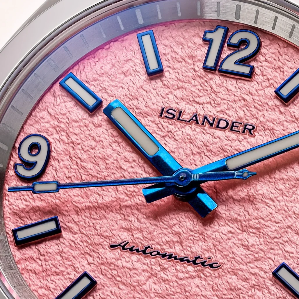 Close-up: Islander automatic watch. Crinkled pink dial, blue luminous hands, white/blue markers & numerals 9, 12.