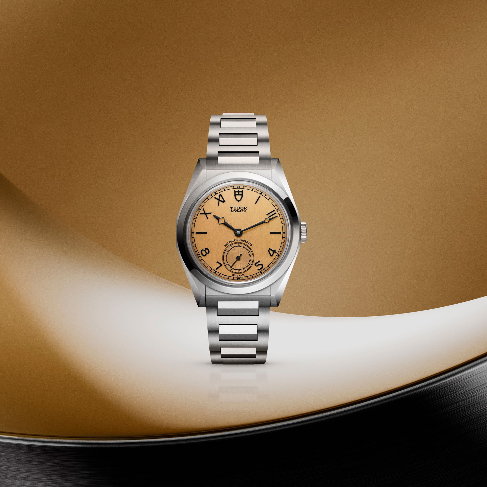 Silver Tudor Monarch watch with salmon dial, mixed hour markers, small seconds, on metal bracelet, gold and white background.