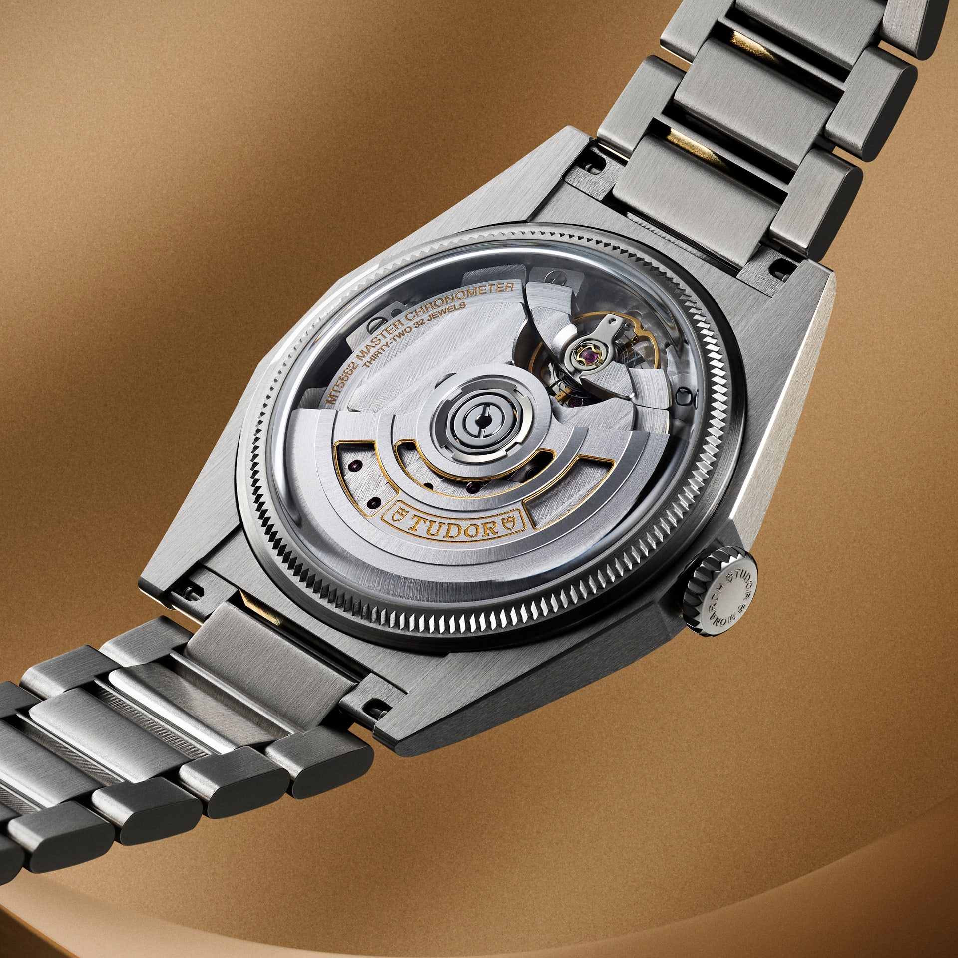 Rear view of a Tudor watch showing its brushed steel case, bracelet, and transparent case back revealing the movement with gold 