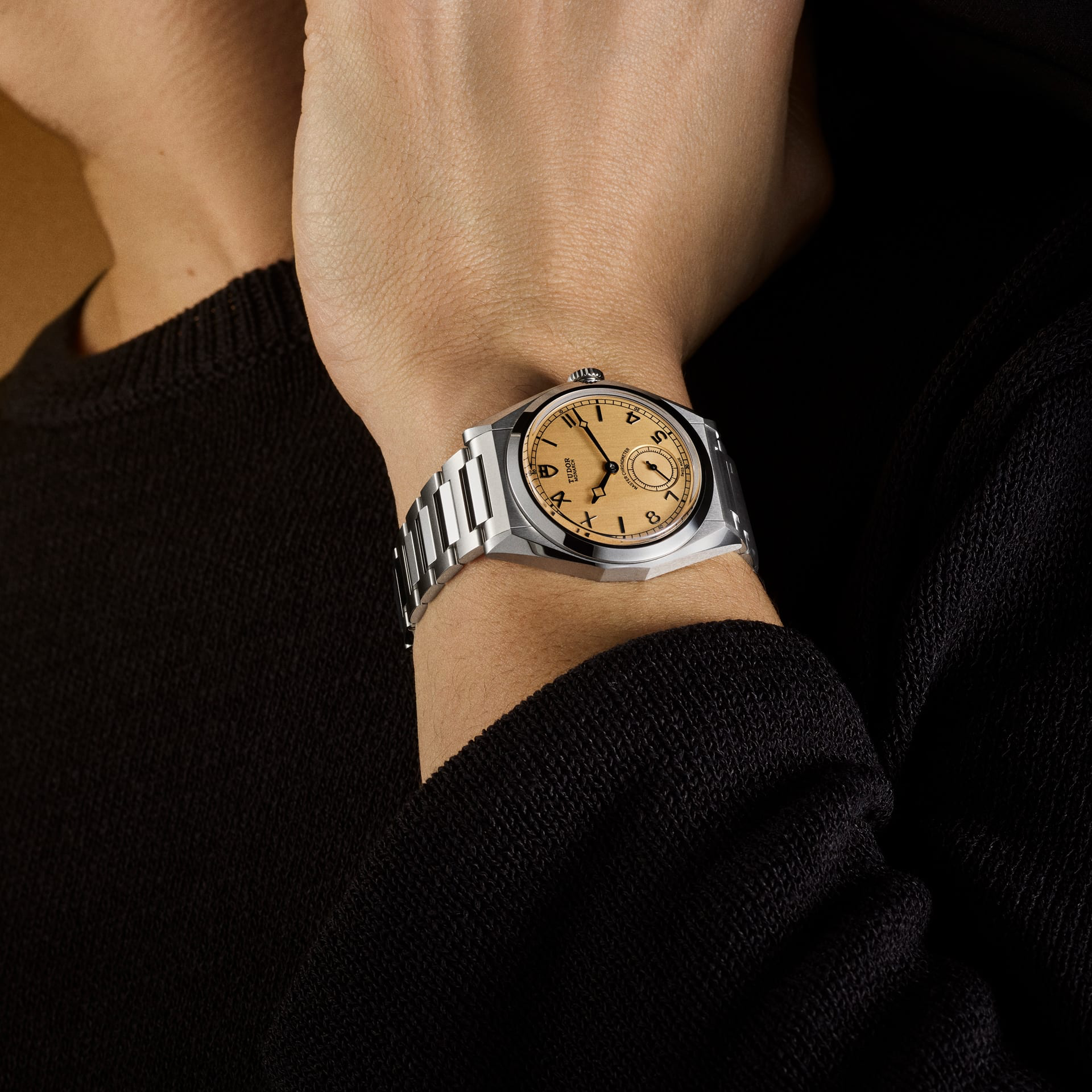 Wrist wearing a steel Tudor Monarch watch with a faceted case, integrated bracelet, and a salmon-colored dial with Roman numerals.