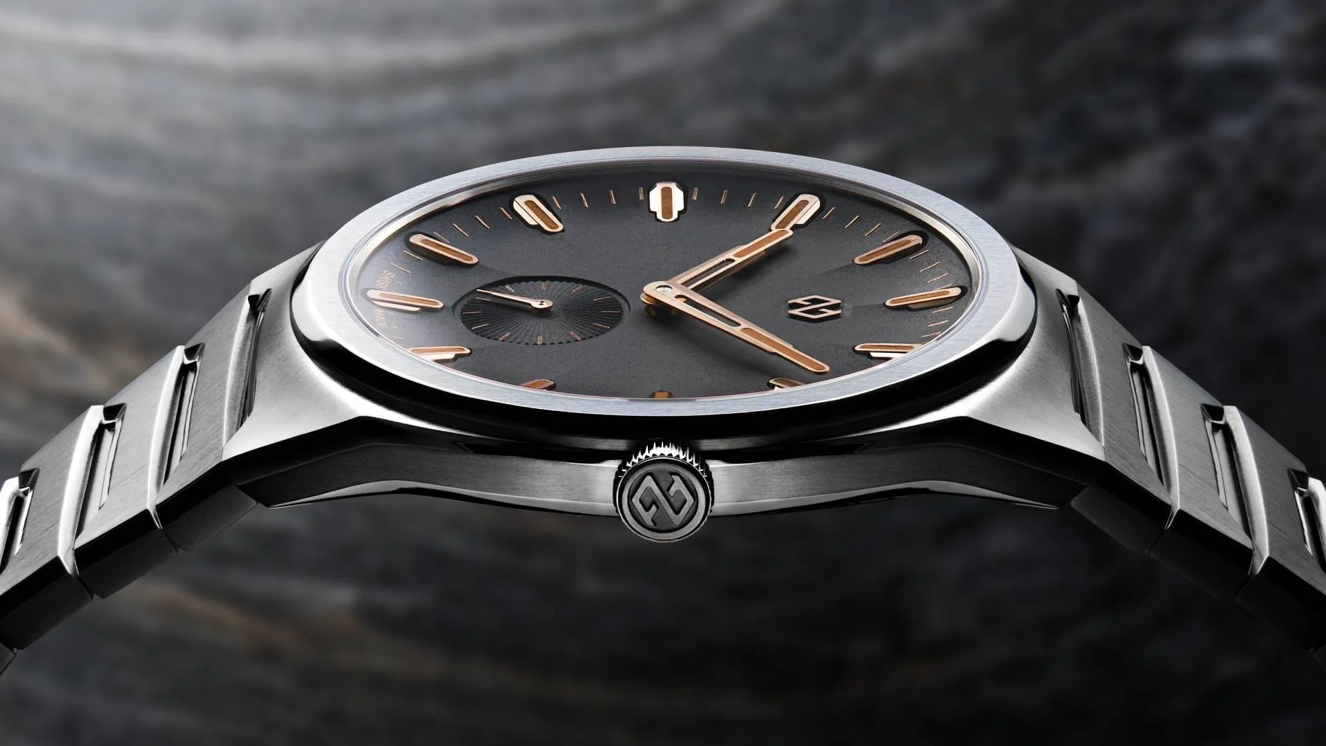Premium brushed steel watch: dark grey dial, rose gold skeleton hands, markers, small seconds, integrated bracelet.