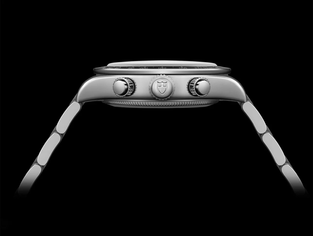 Side profile of a stainless steel Tudor chronograph watch with a metal bracelet against a black background.